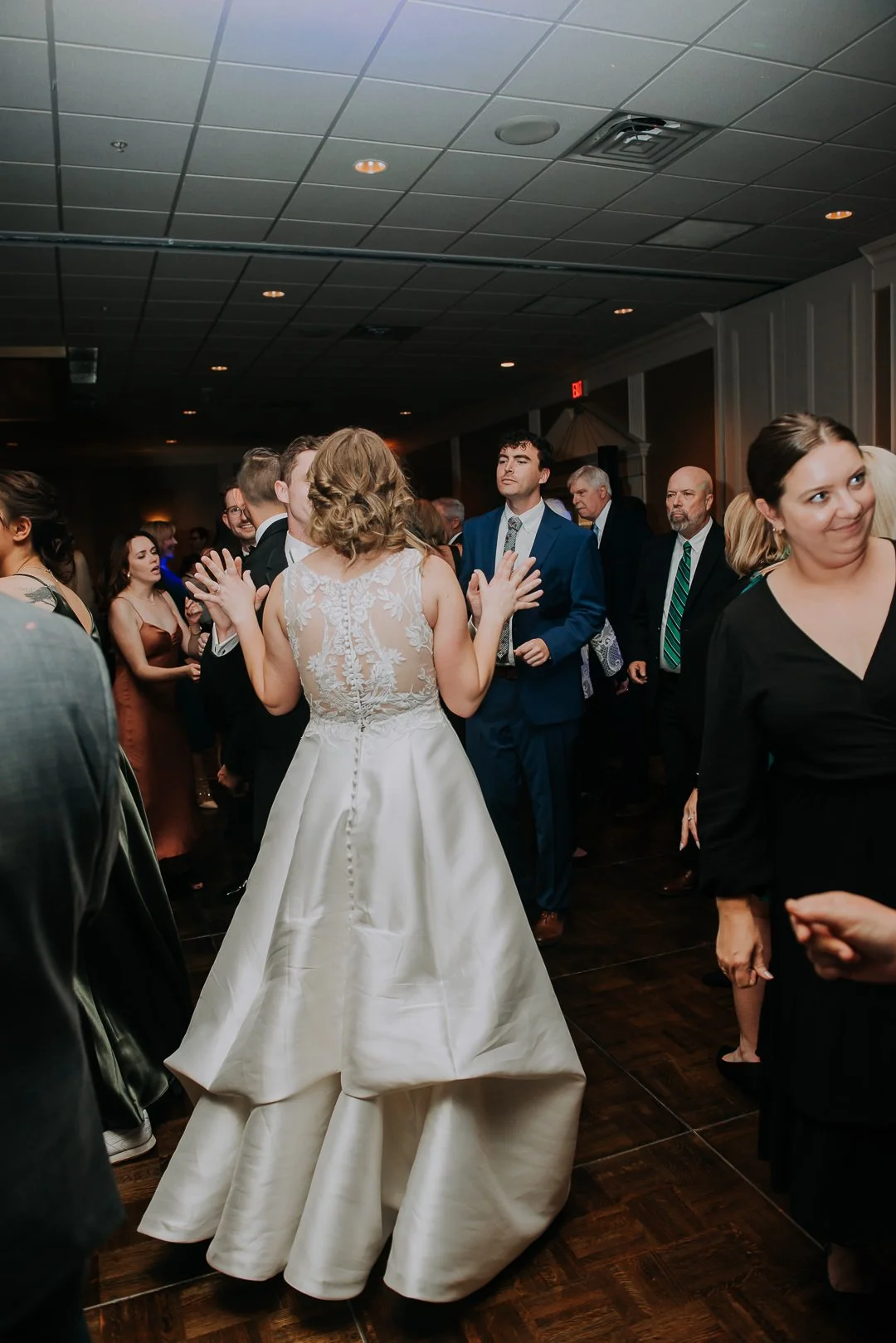 A bride in a white wedding dress dancing at a wedding reception with guests surrounding her.