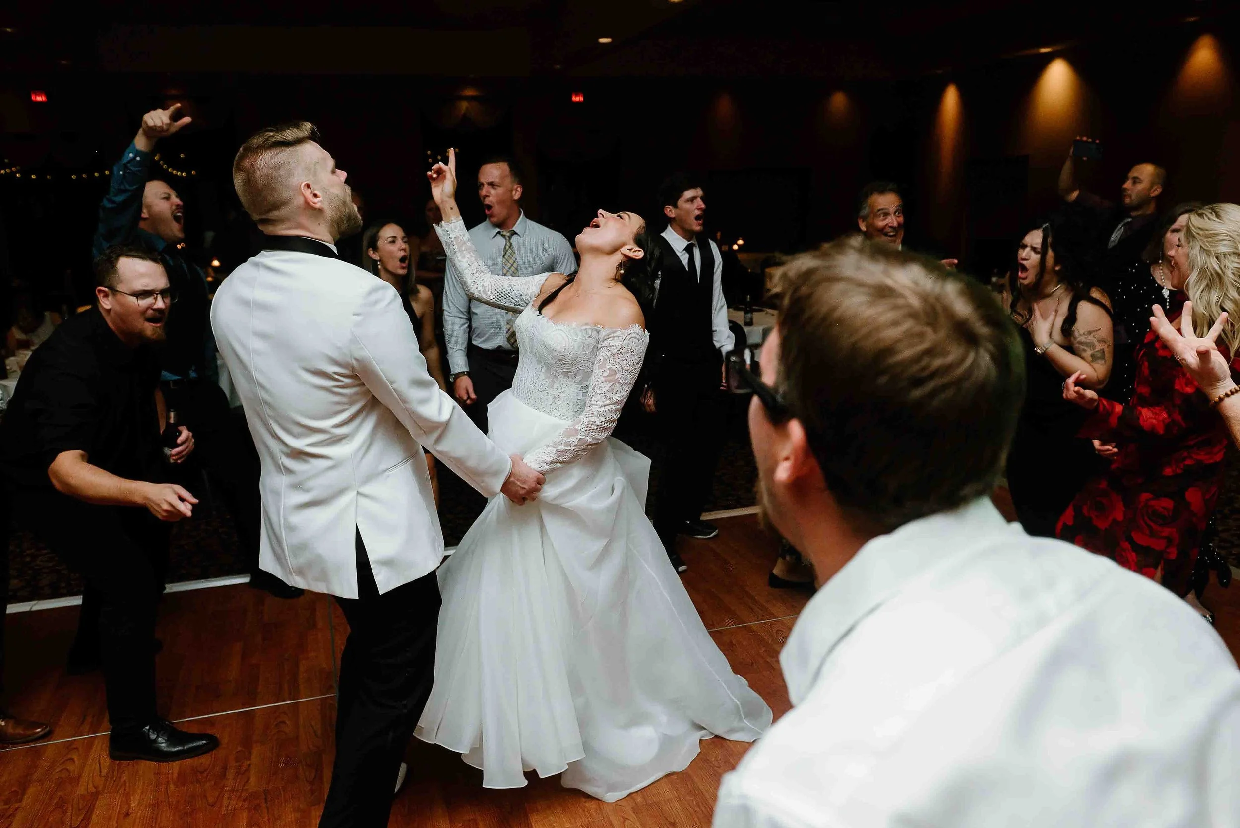 A bride and groom dancing at their wedding reception, surrounded by friends and family cheering and celebrating.