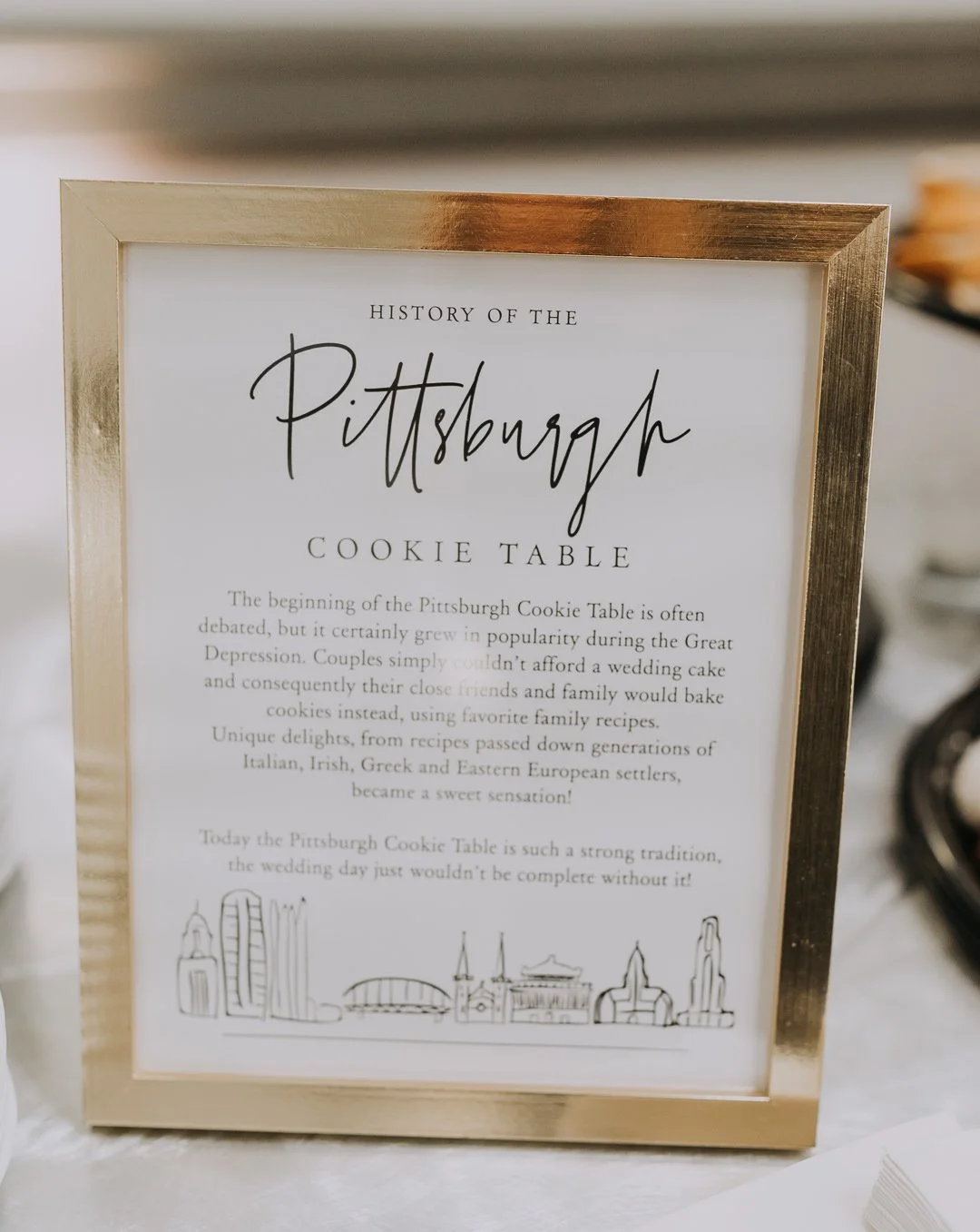 Sign titled 'History of the Pittsburgh Cookie Table' with a brief history and a line drawing of Pittsburgh landmarks.