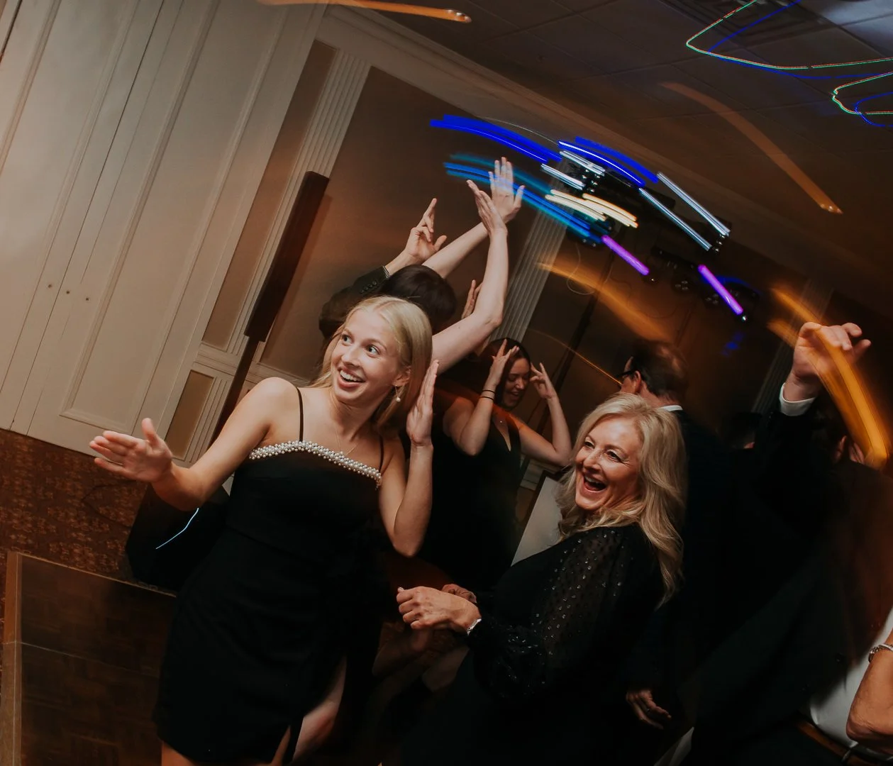 People dancing and having fun at a lively celebration or party, with colorful lights and blurred motion indicating energetic movement.