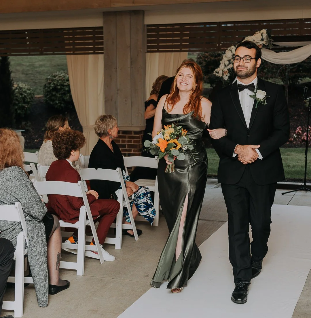 A bride and groom walking down the aisle at their wedding ceremony, with seated guests watching.