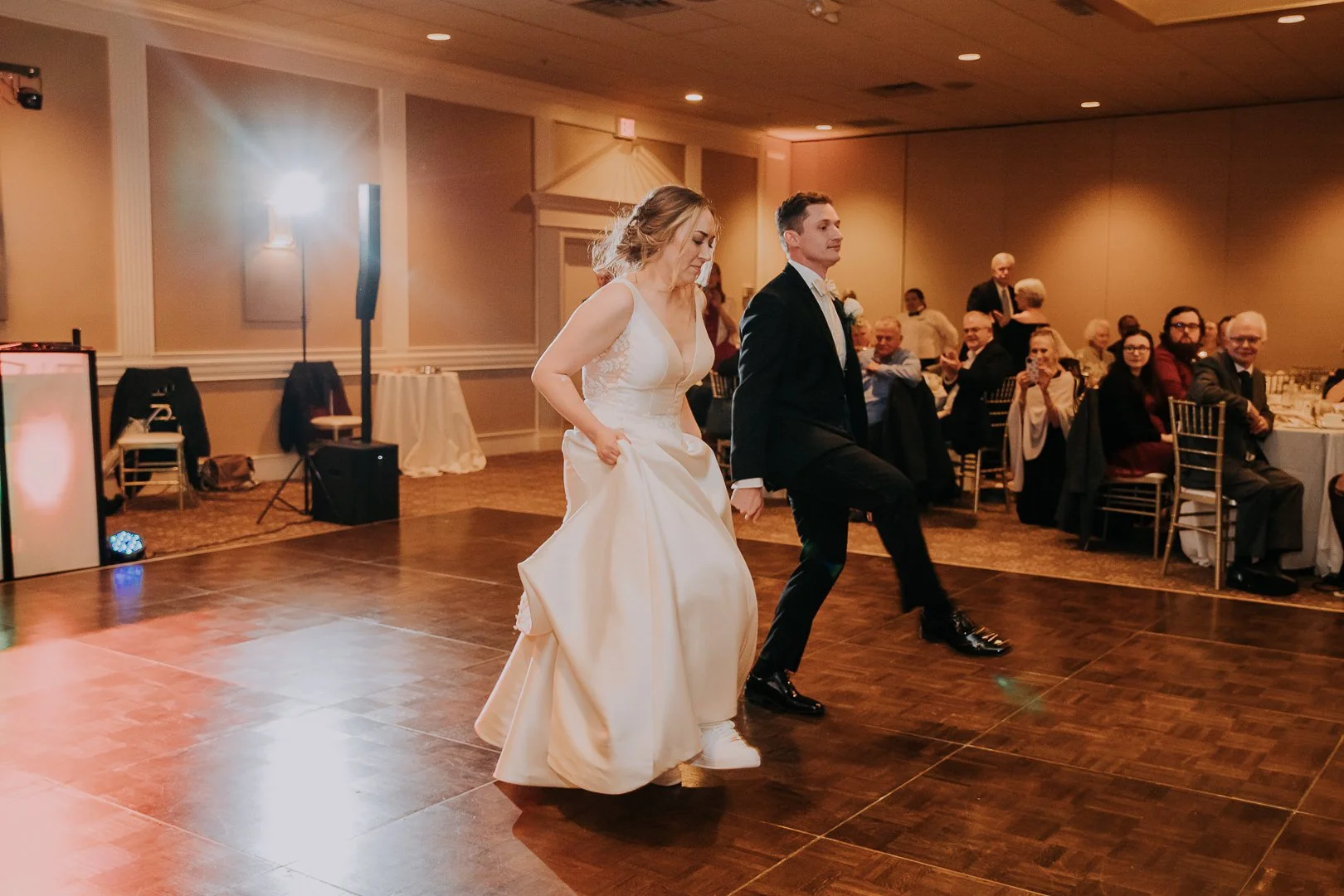Bride and groom dancing at their wedding reception, with seated guests watching and smiling in the background.