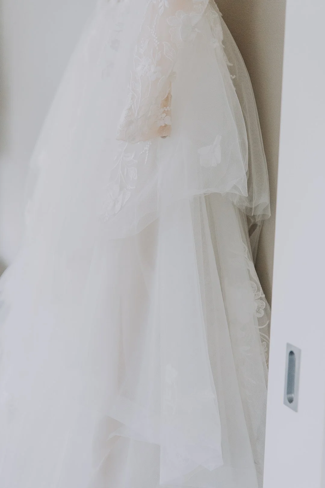 Close-up of a white wedding dress with lace and tulle fabric hanging on a door.