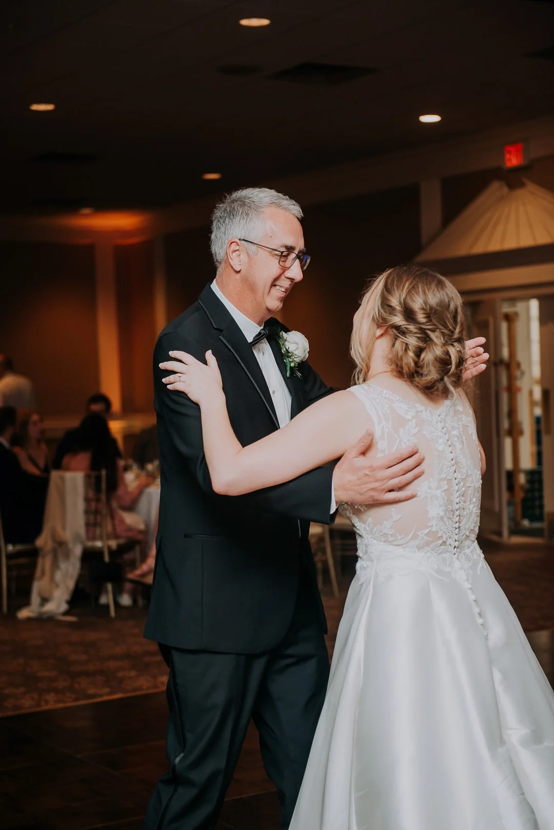 A bride and an older man dancing together at a wedding reception in a dimly lit banquet hall.