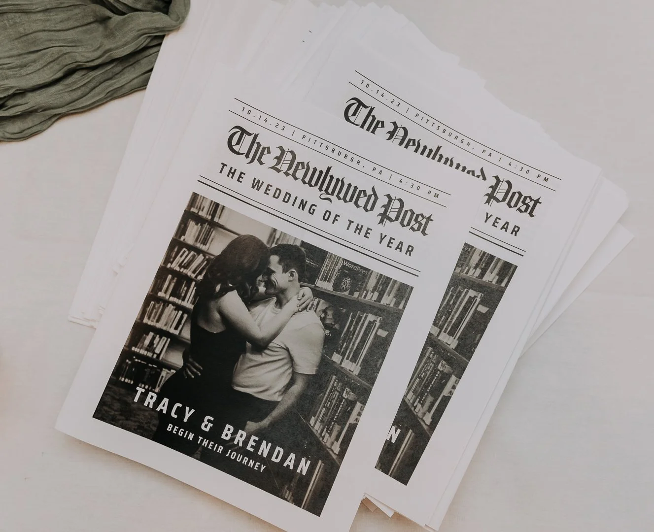 A printed newspaper titled 'The Pittsburgh Post' announcing the wedding of Tracy and Brendan, with a black and white photo of the couple embracing in a library, and details about the wedding date and time.