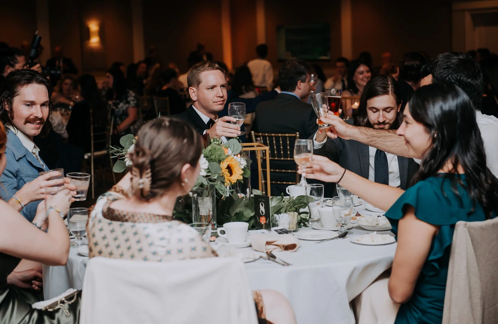 People gathered around a table at a formal event, raising glasses in a toast, with a floral centerpiece and elegant table settings.