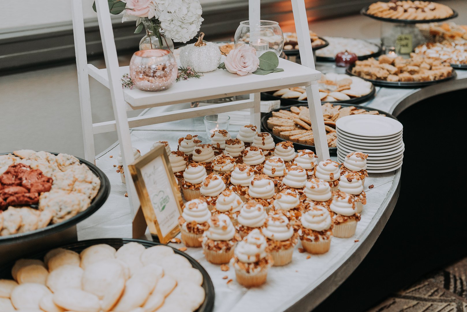 Table set with various desserts including cupcakes, cookies, and pies, decorated with flowers and pumpkins for a celebration.