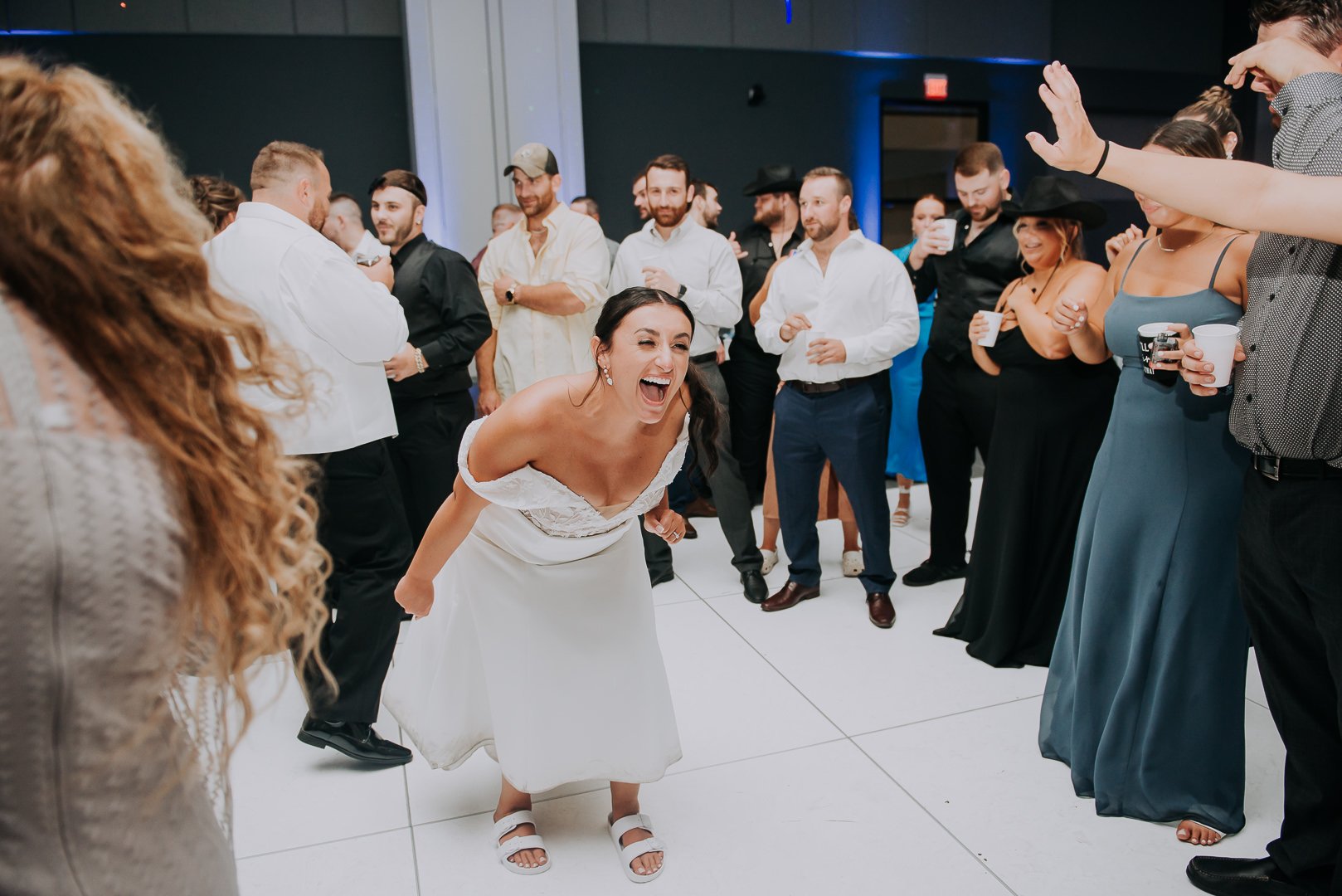 A woman in a white dress is playfully leaning forward and laughing at a wedding reception.