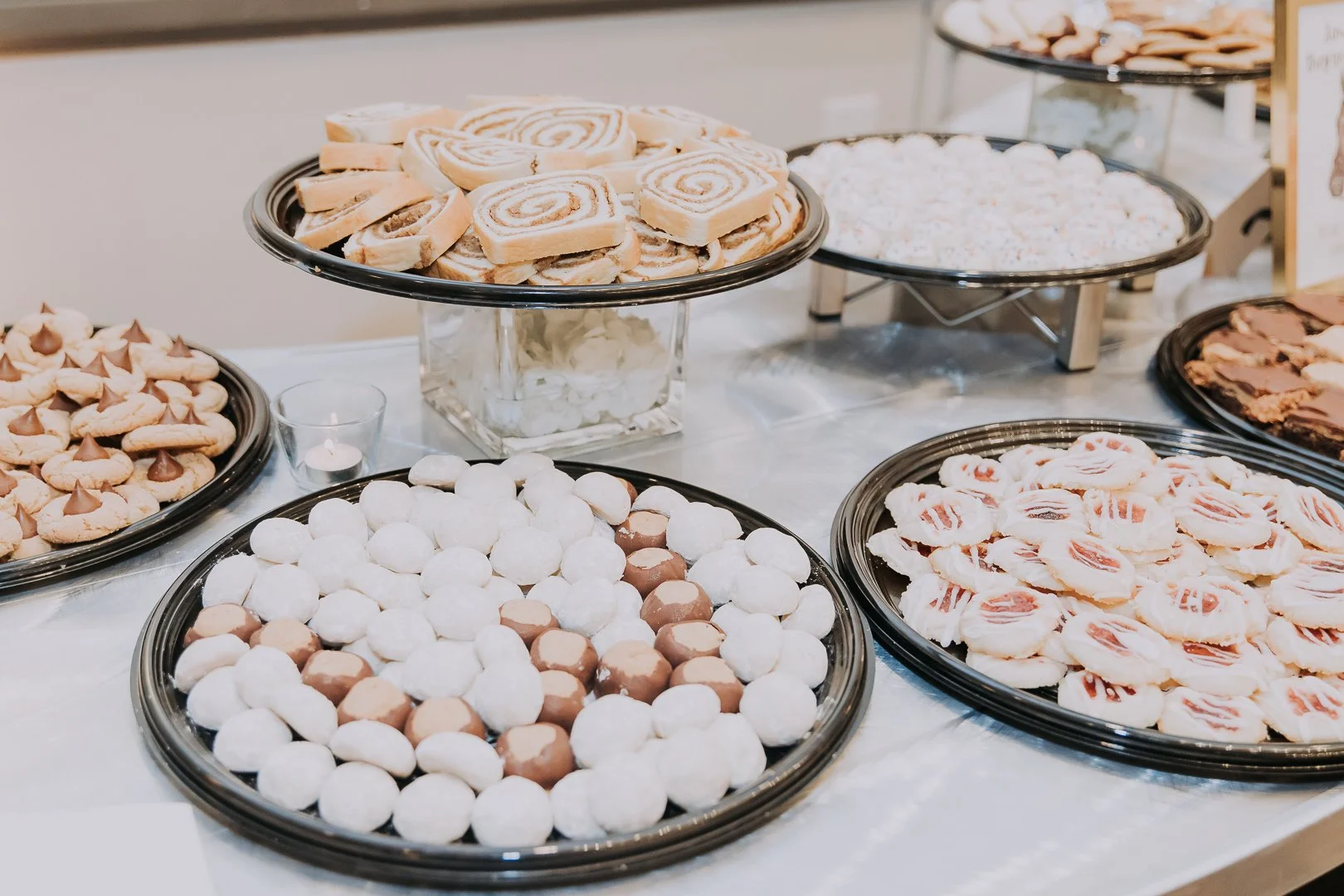 Assorted cookies and chocolates displayed on black serving trays at a dessert table.
