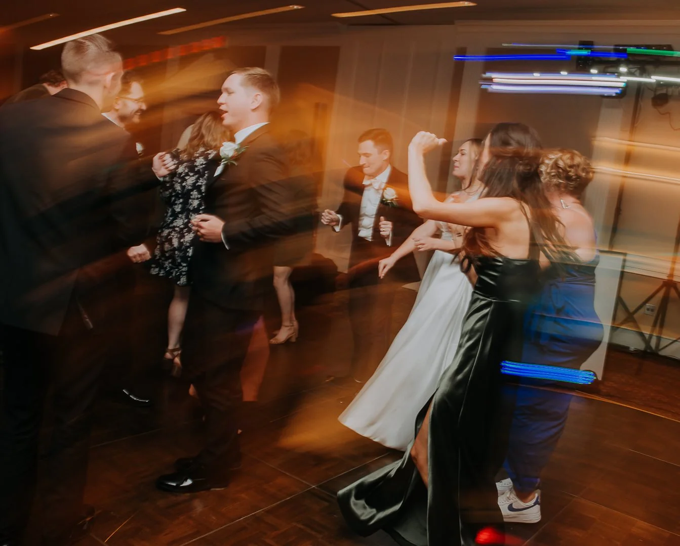 People dancing at a wedding reception with colorful motion blur effects.