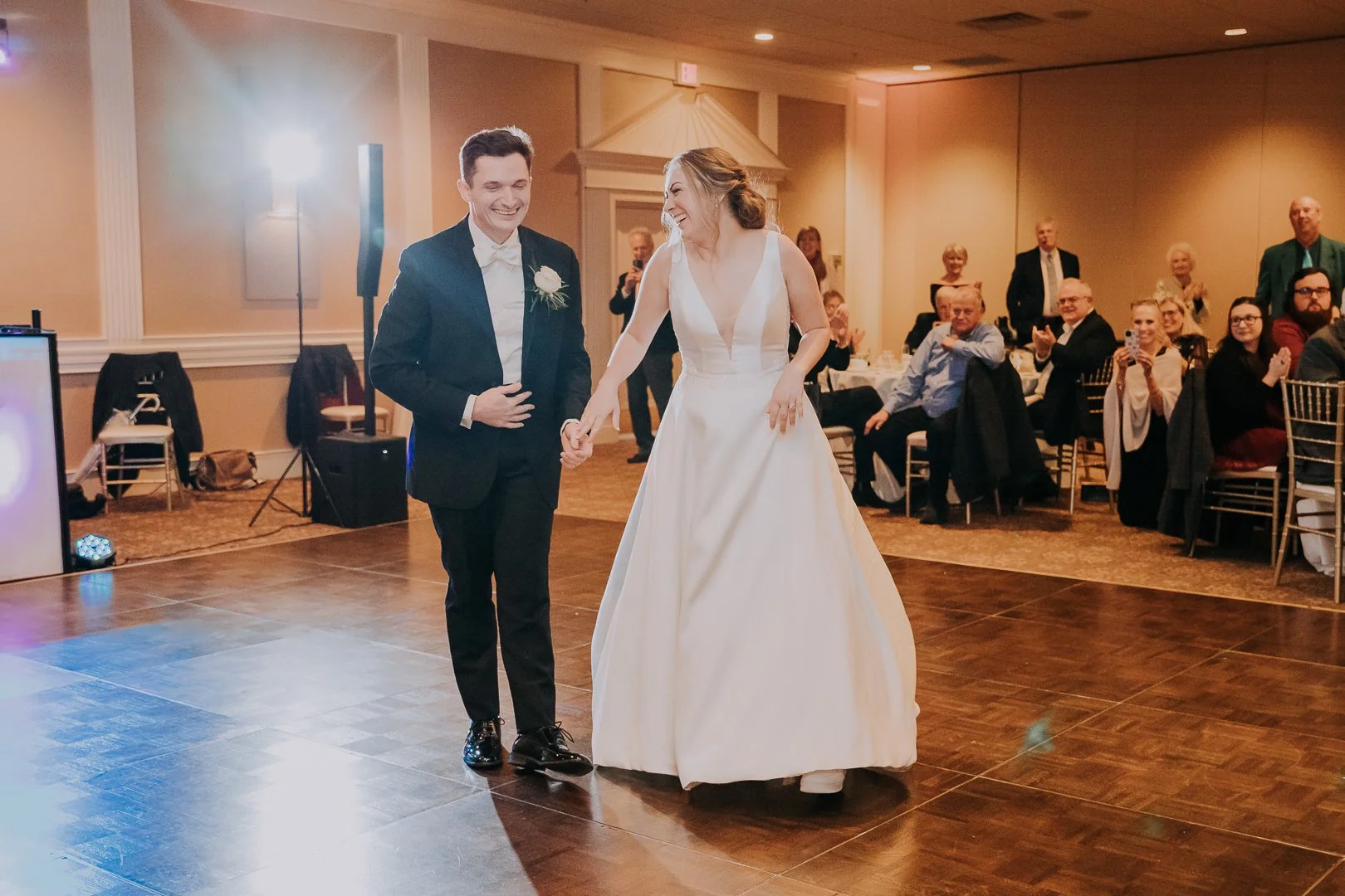 Bride and groom dancing at a wedding reception, with guests seated at tables in the background, in an elegant banquet hall.