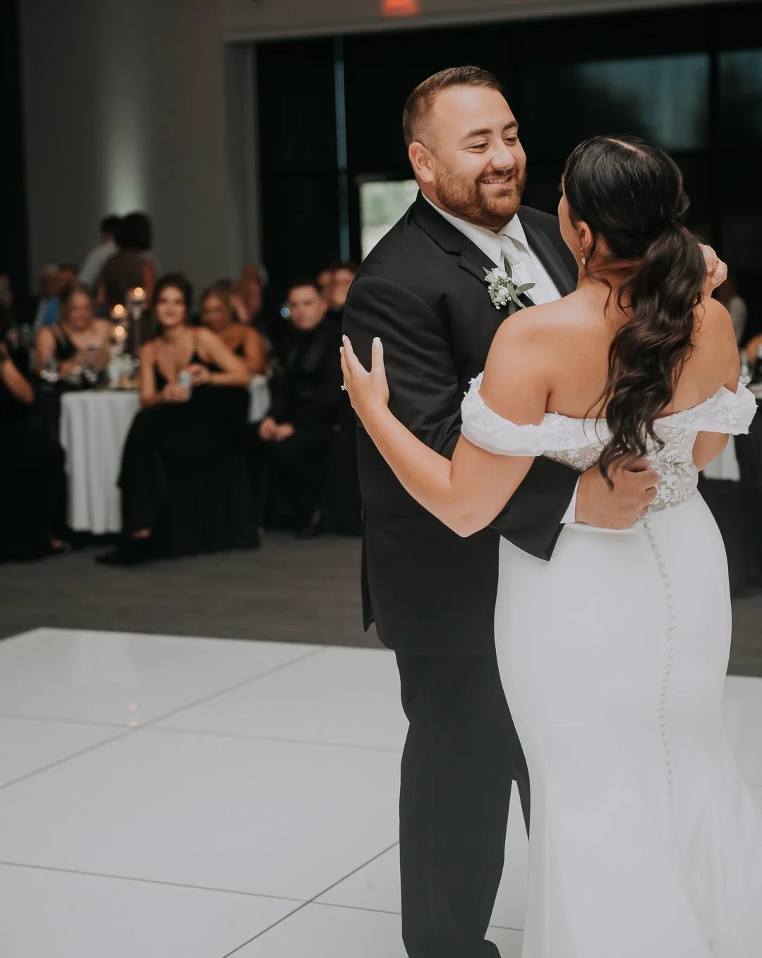 A bride and groom sharing their first dance at their wedding reception, with guests sitting at tables in the background.