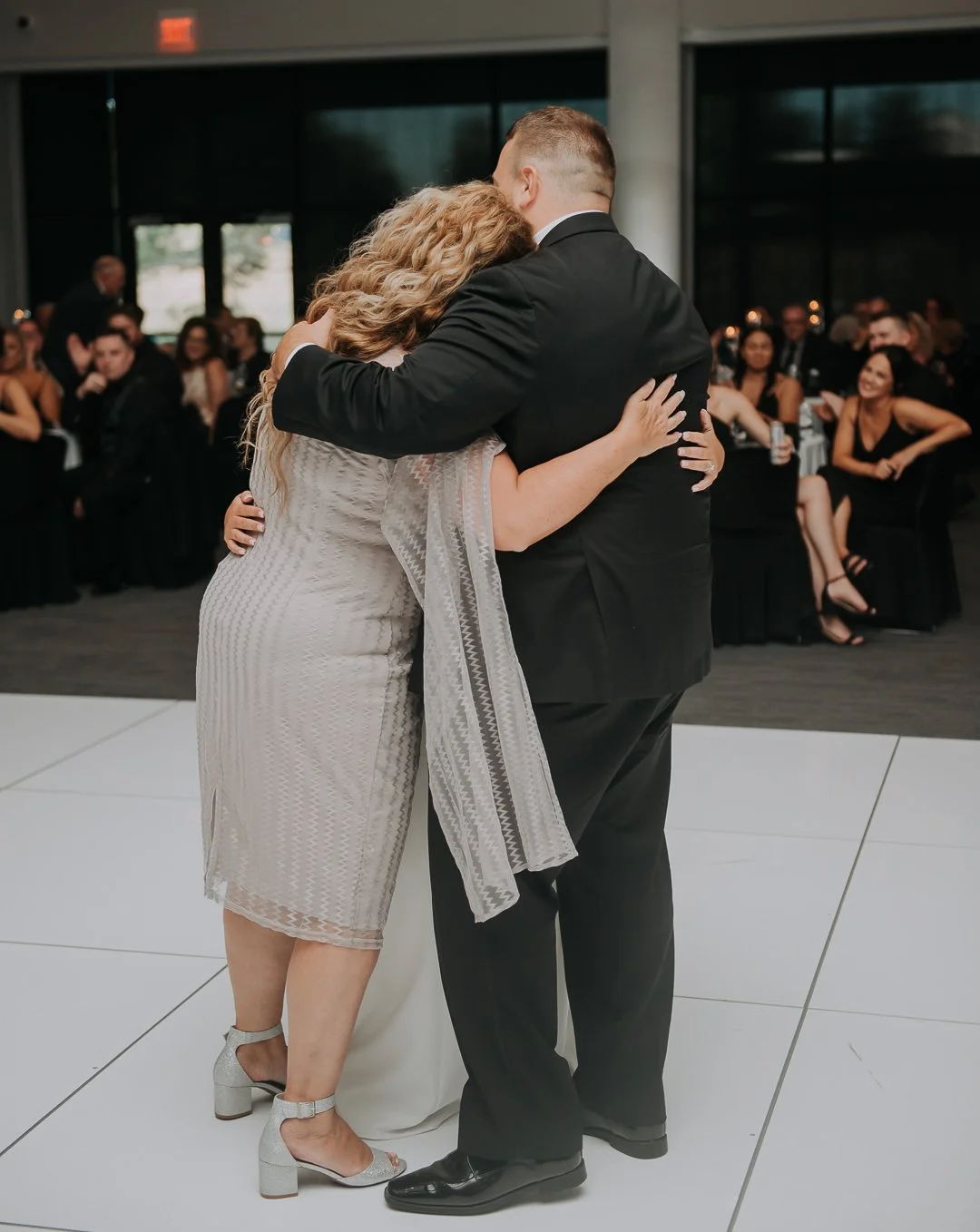 A couple sharing a hug on the dance floor at a wedding reception with guests seated at tables watching.