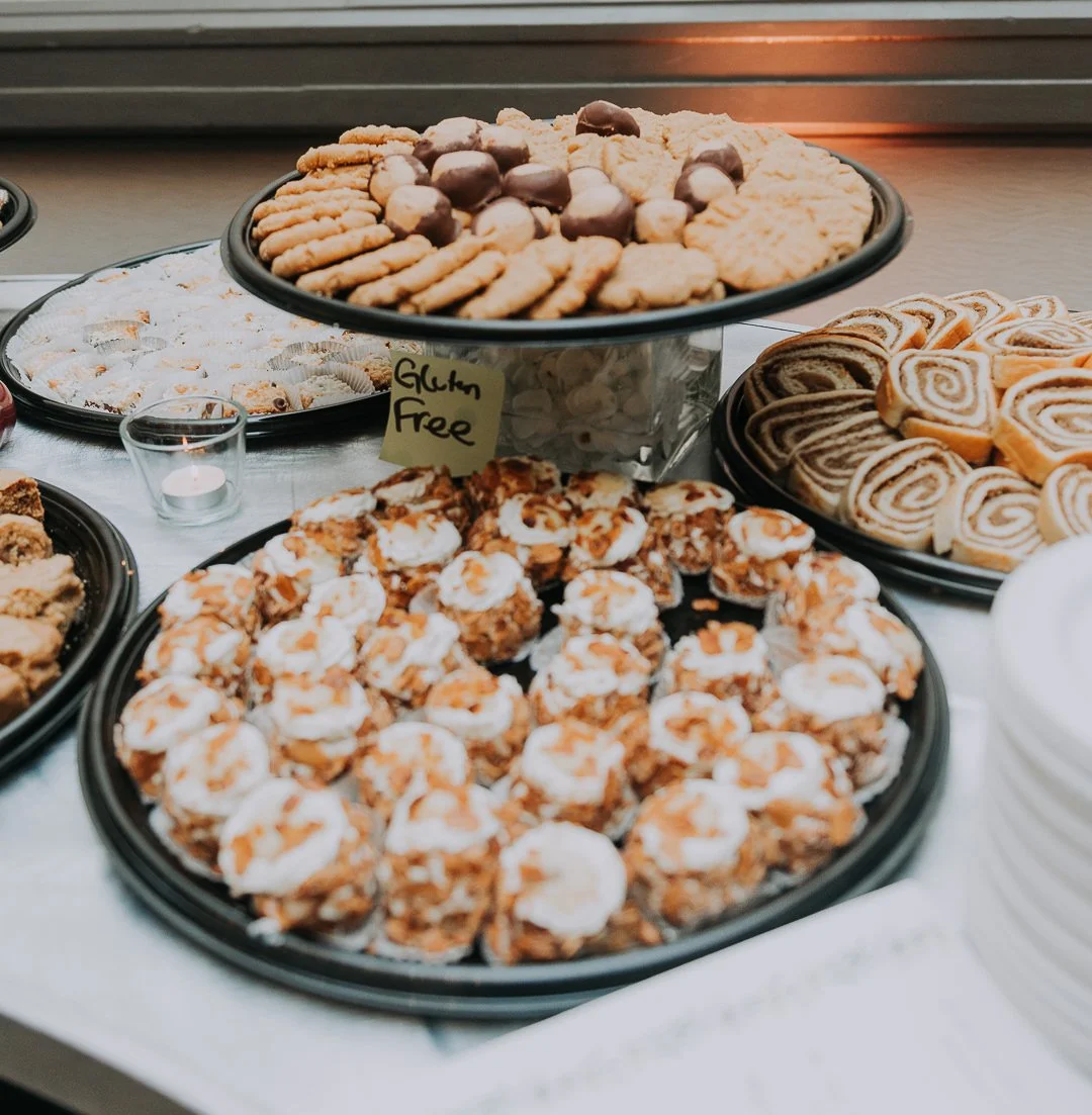 Assorted cookies and snacks on a tray, including gluten-free cookies, wrapped in white icing, cinnamon rolls, and chocolate-covered cookies.