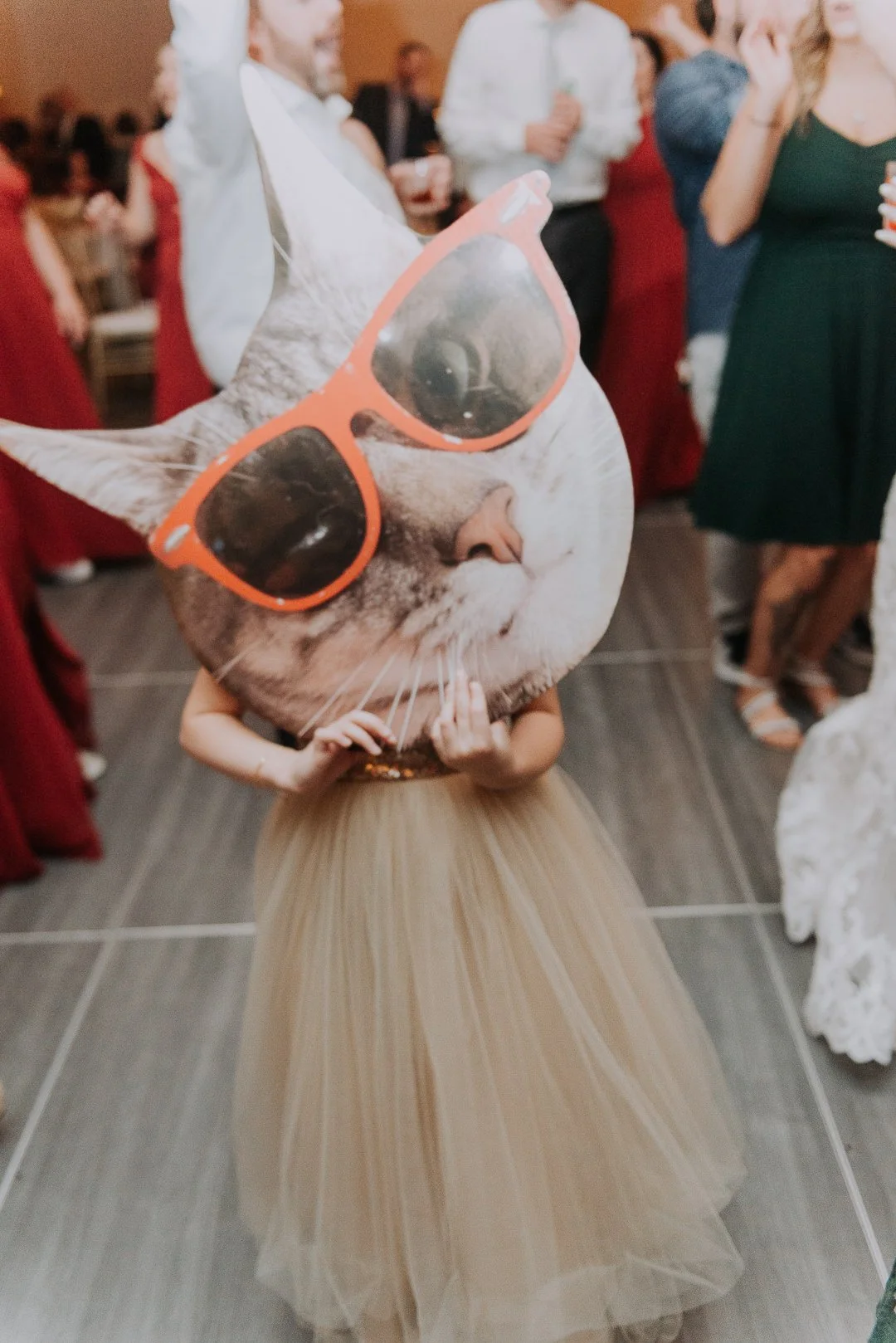 Person wearing a dress holding a large cat face mask with sunglasses at a party or celebration.