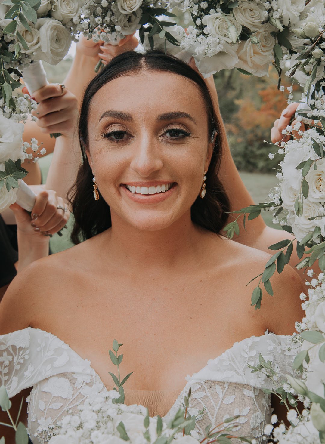 A bride smiling inside a floral frame made of white roses and greenery.