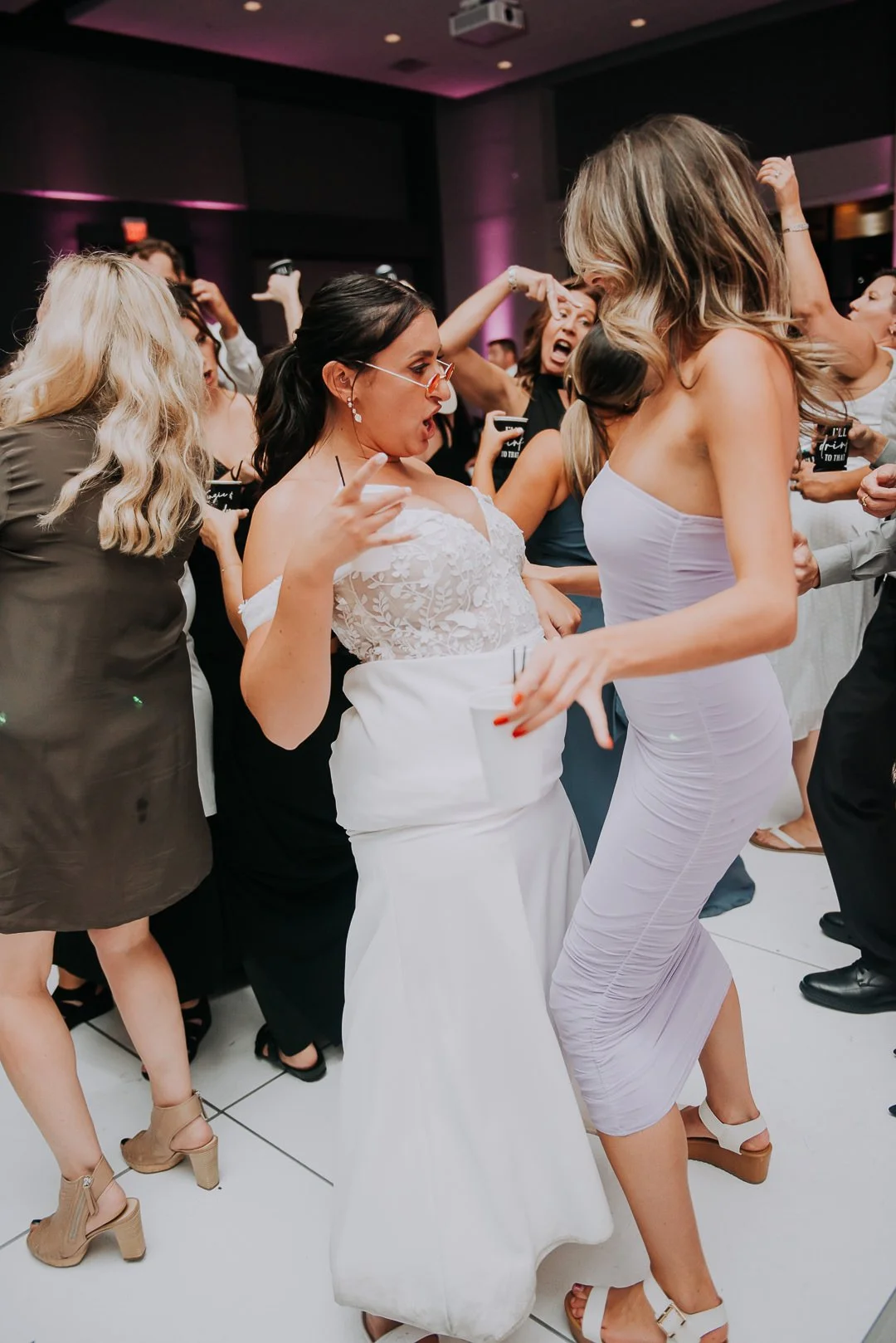 People dancing and having fun at a celebration event, possibly a wedding reception, with women in dresses and lively expressions.