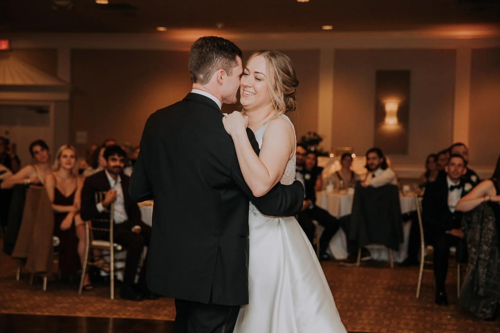 A bride and groom sharing their first dance at their wedding reception, surrounded by seated guests.