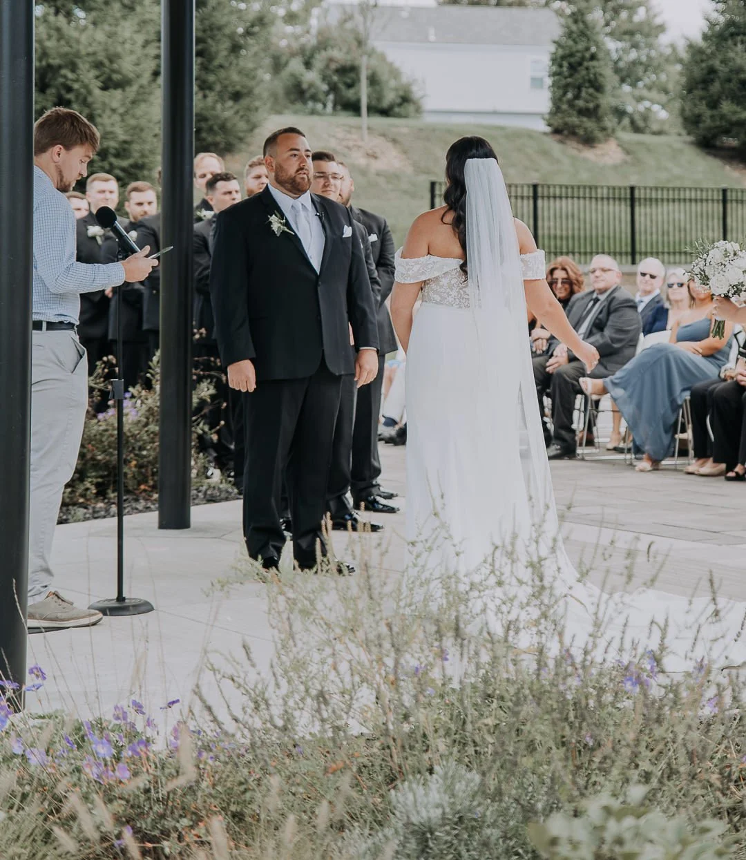Bride and groom standing during outdoor wedding ceremony with guests seated in the background.