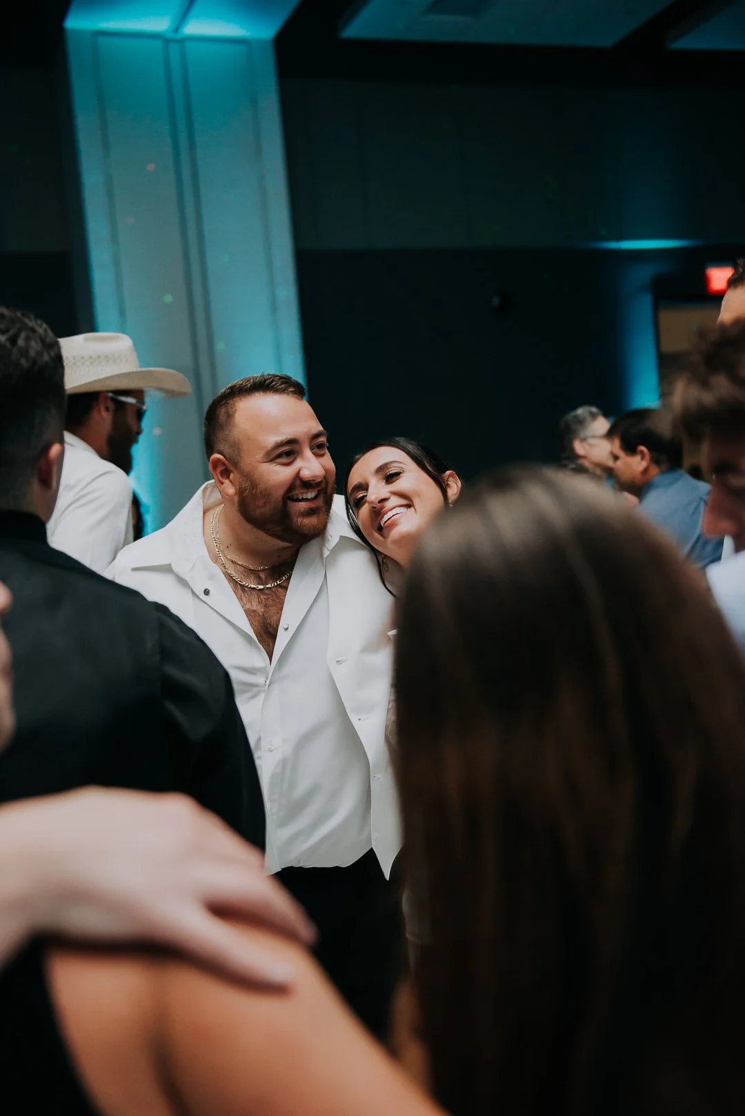 A group of people at a party, with a man and woman smiling and leaning close to each other at the center.