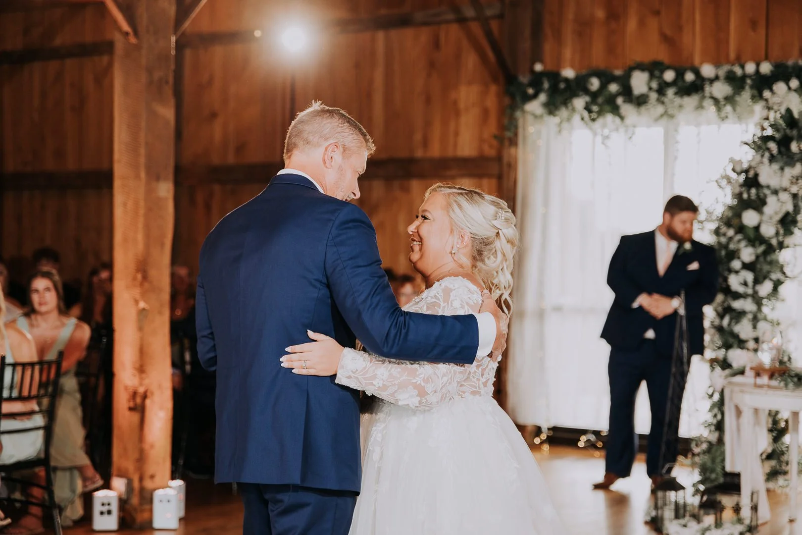 A bride and groom sharing their first dance at a wedding reception in a wooden venue with floral decorations.
