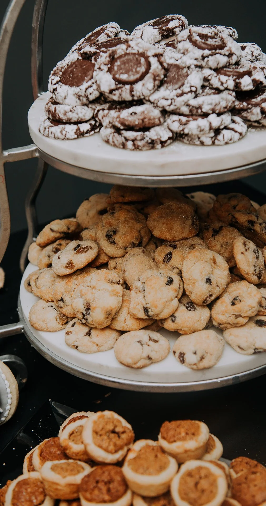 Assorted cookies including chocolate chip and powdered sugar cookies displayed on tiered trays.