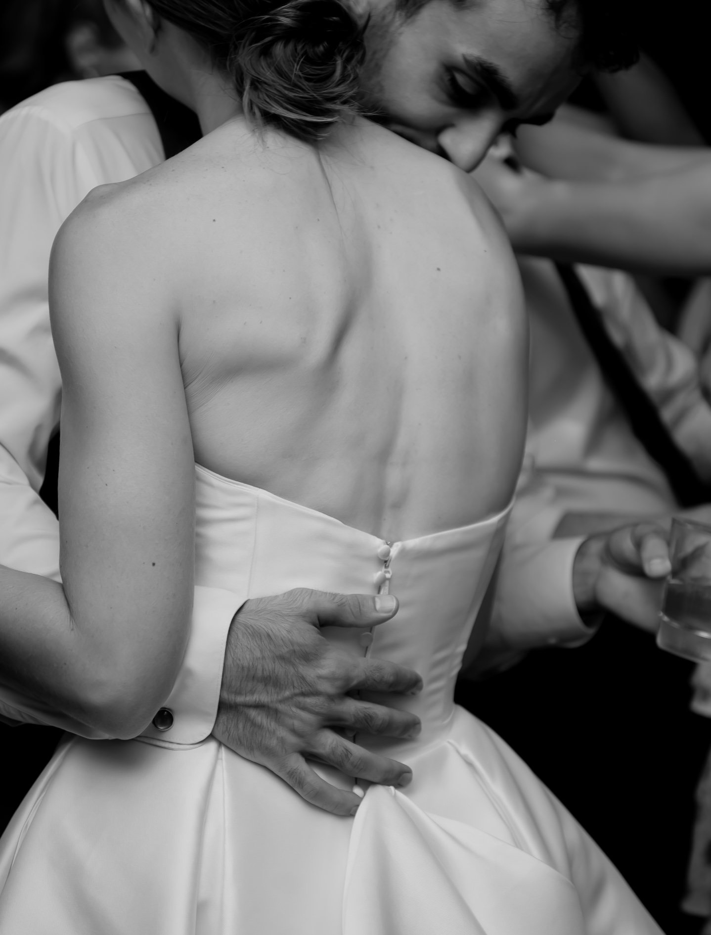 A close-up black and white photo of a woman in a strapless dress with her head resting on another person's shoulder, showing her back and shoulders.