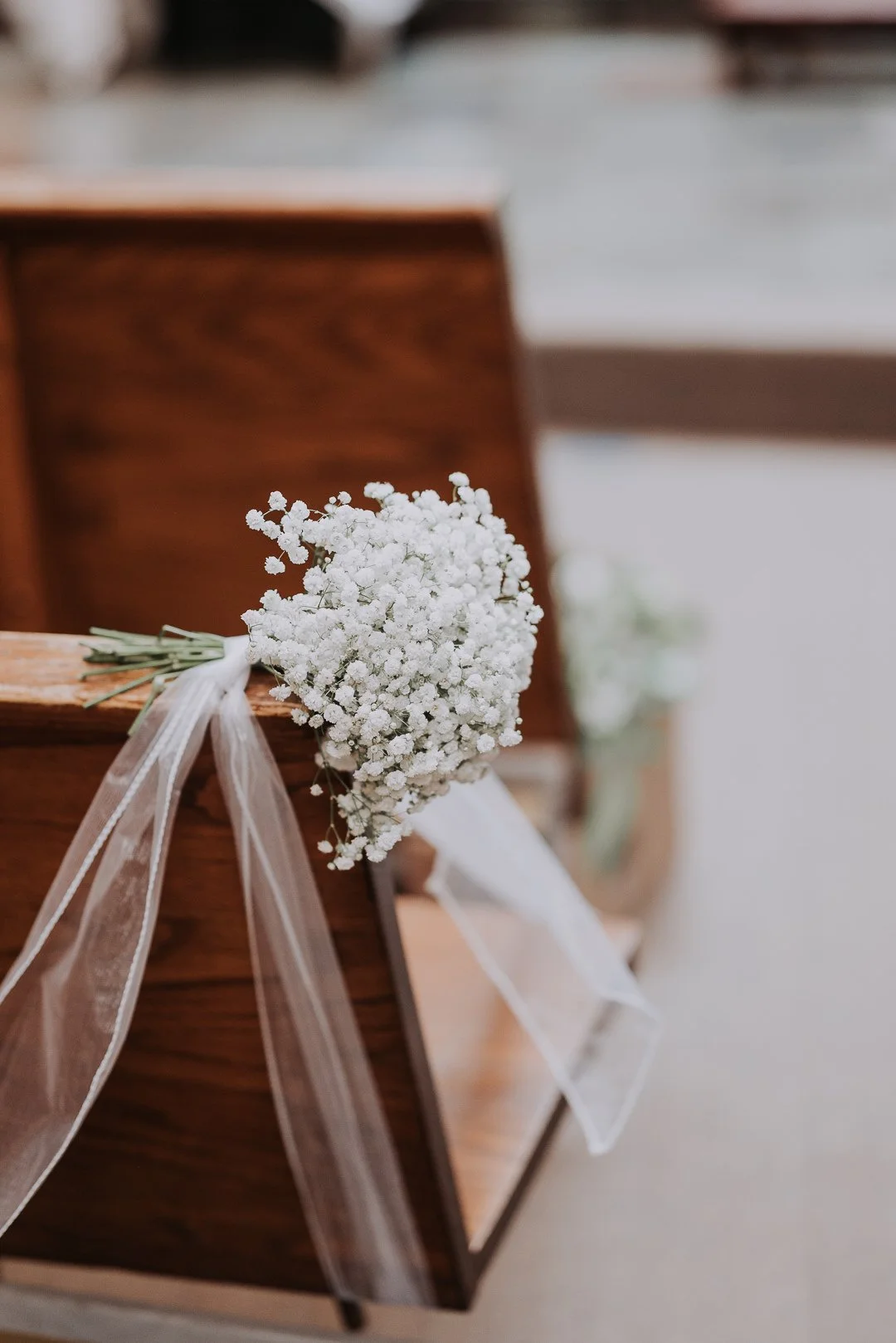 A small bouquet of white baby's breath flowers attached to a wooden church pew with a white ribbon during a wedding ceremony.