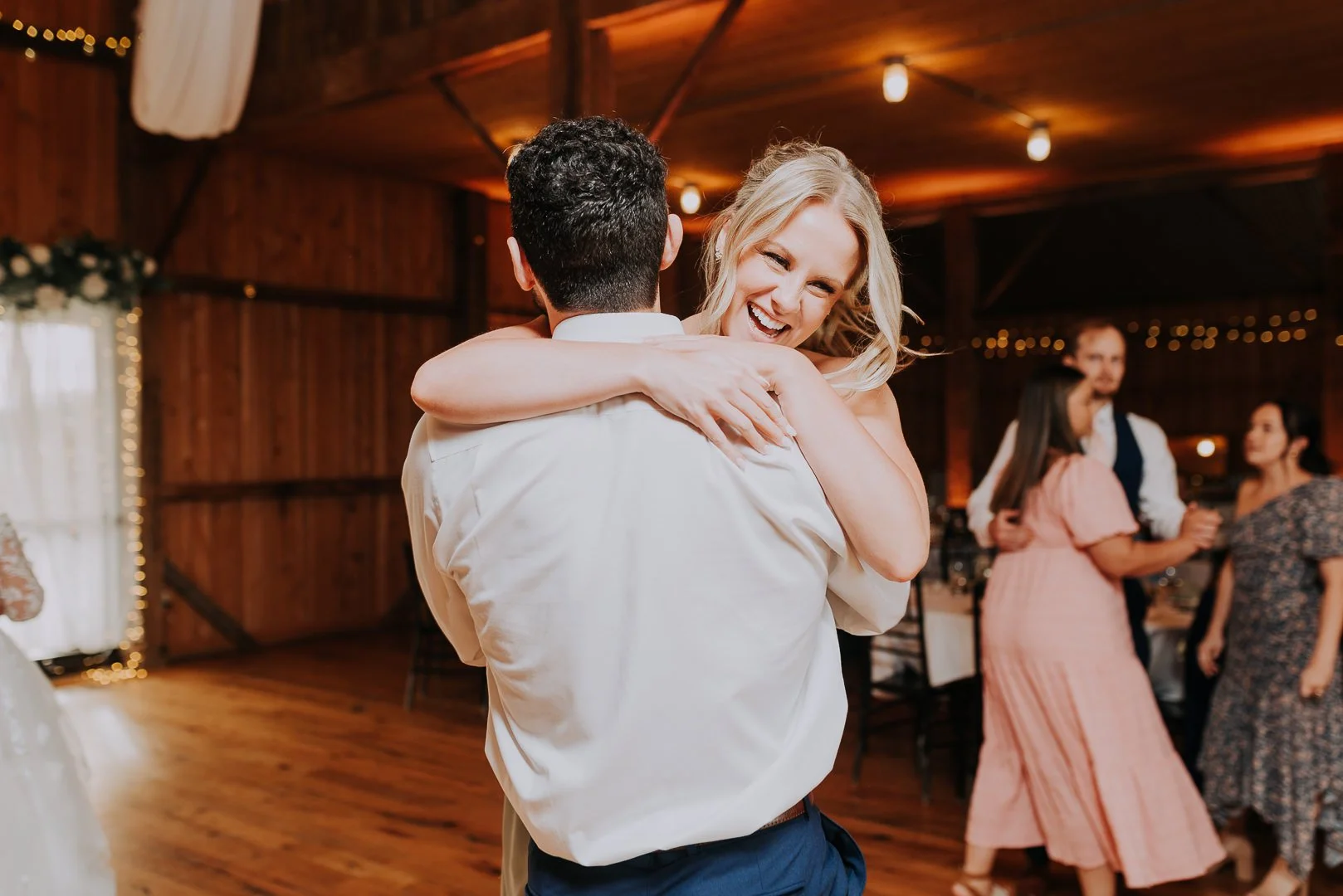A couple dancing at a wedding reception, with the woman smiling and hugging the man