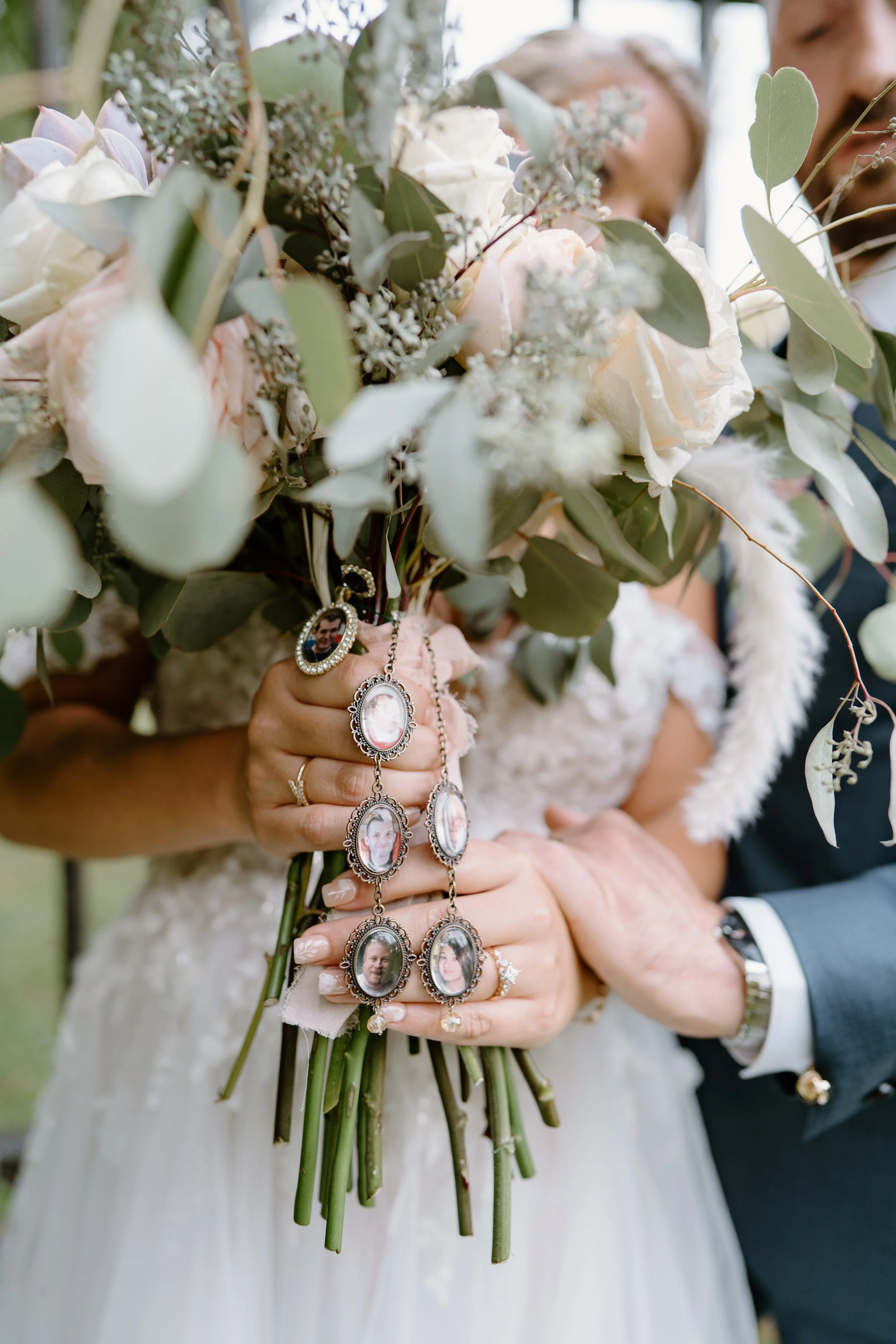 Bride holding a bouquet with family photo charms, with groom's hand on her hand, during a wedding ceremony.