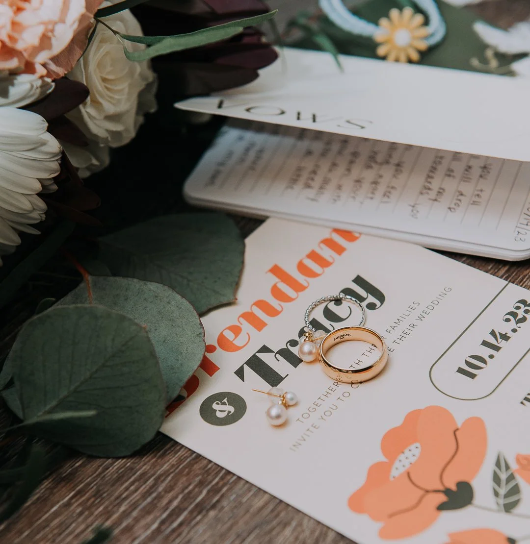 Invitation to a wedding with jewelry and flowers on a wooden surface.