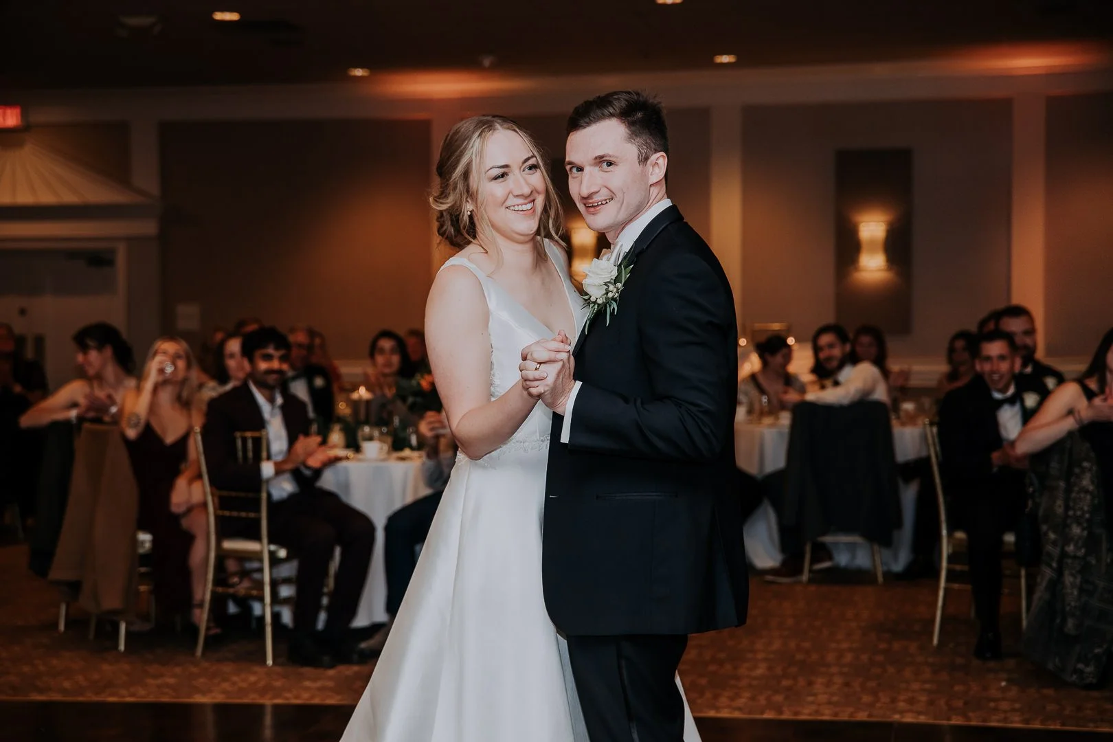A bride and groom sharing their first dance at a wedding reception, surrounded by seated guests.