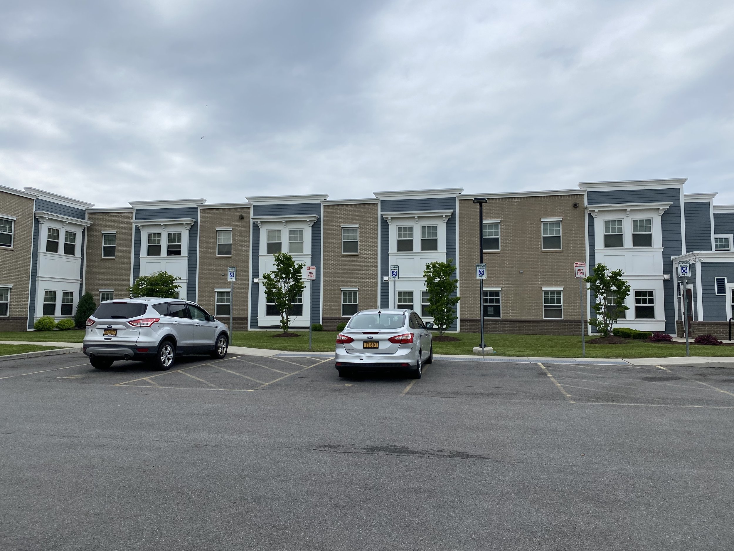 Apartment complex with three parked cars in the foreground and a partly cloudy sky overhead.