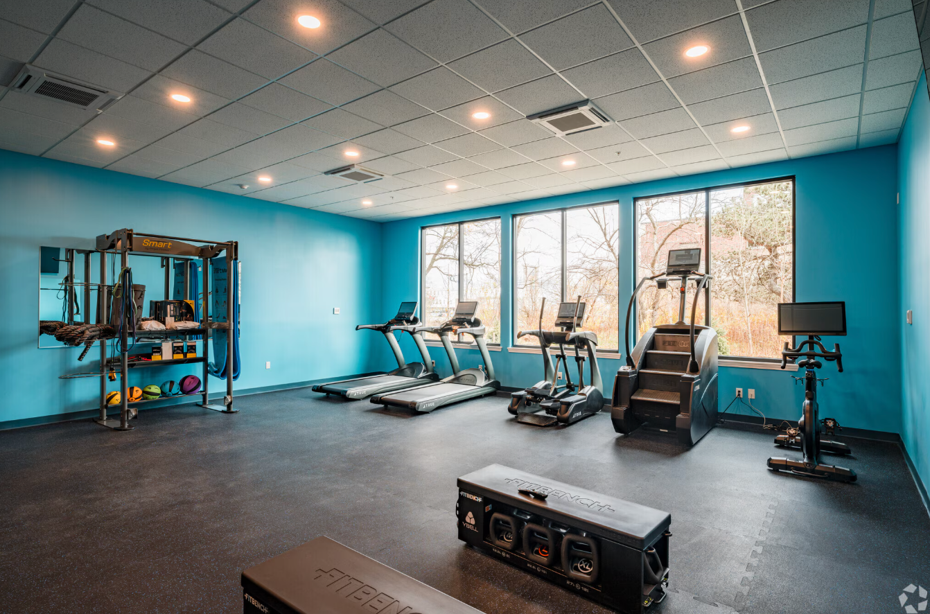 apartment complex gym with blue walls, treadmills, Stairmaster, bike, and weight rack
