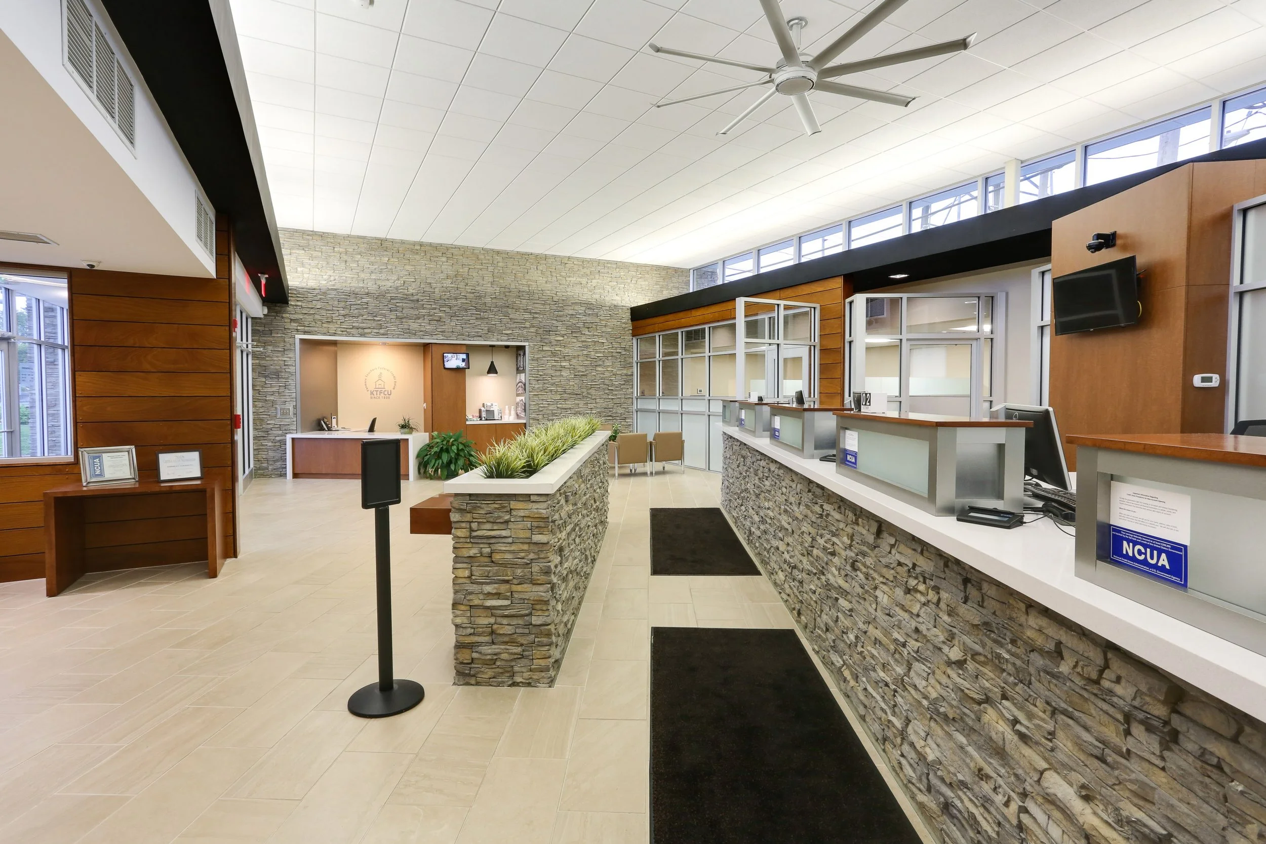 Empty front desk area of a modern office or reception area with stone and wood accents, computer stations, and a ceiling fan.