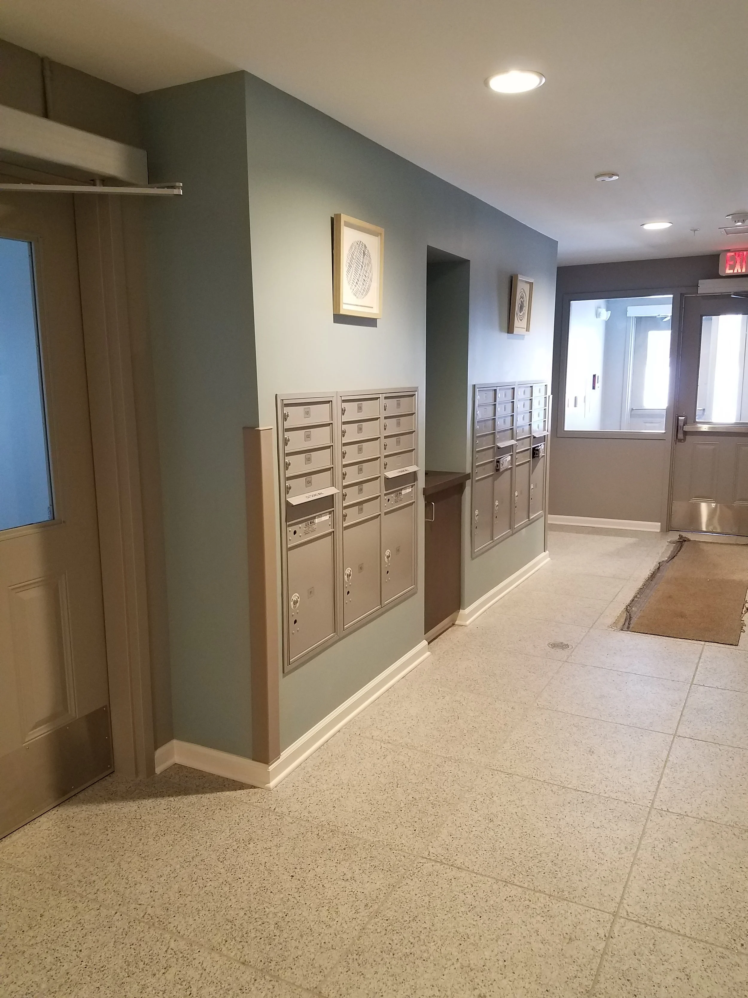 Indoor building lobby with mailboxes on the wall, a door, and exit sign.