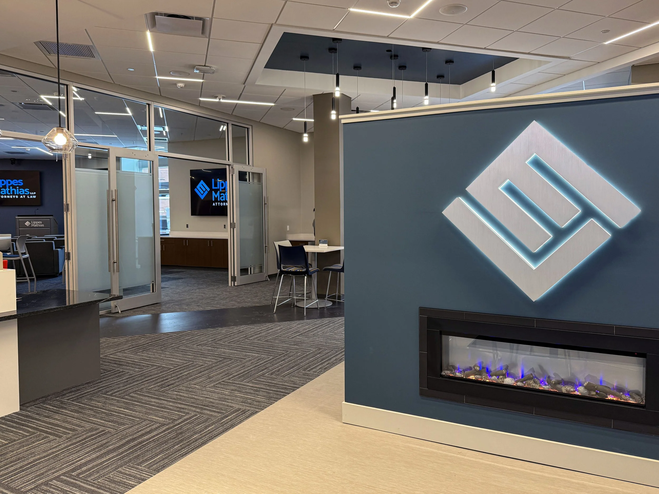 Lippes Mathias entryway with lit up logo over a fire place and a large room with tables in the background