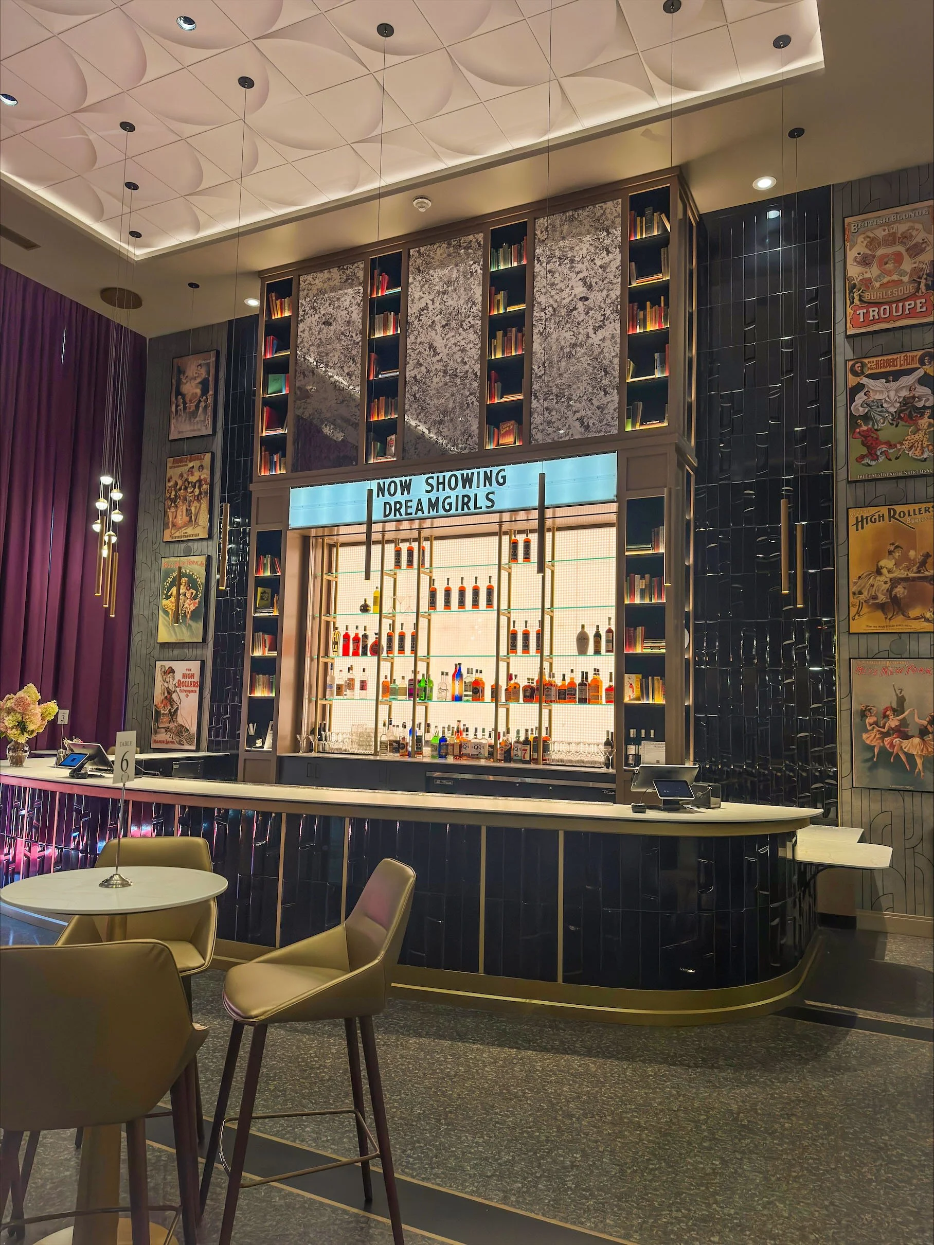 2 story bar with floor to ceiling book cases and light up sign that says "now showing dreamgirls" and vintage theatre posters. Shea's 710 theatre bar area in Buffalo, New York