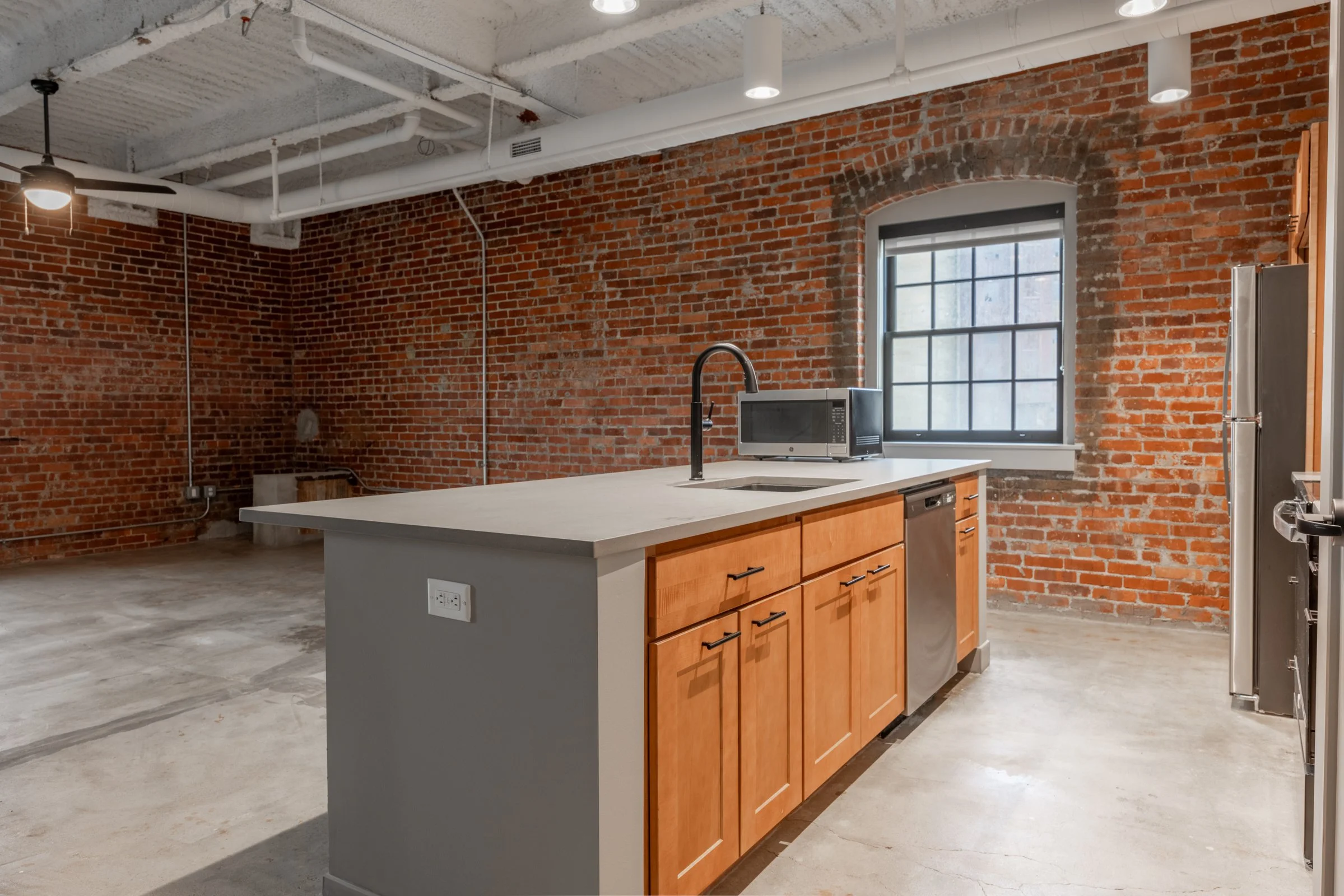 empty kitchen with brick walls, black sinks, and gray counters