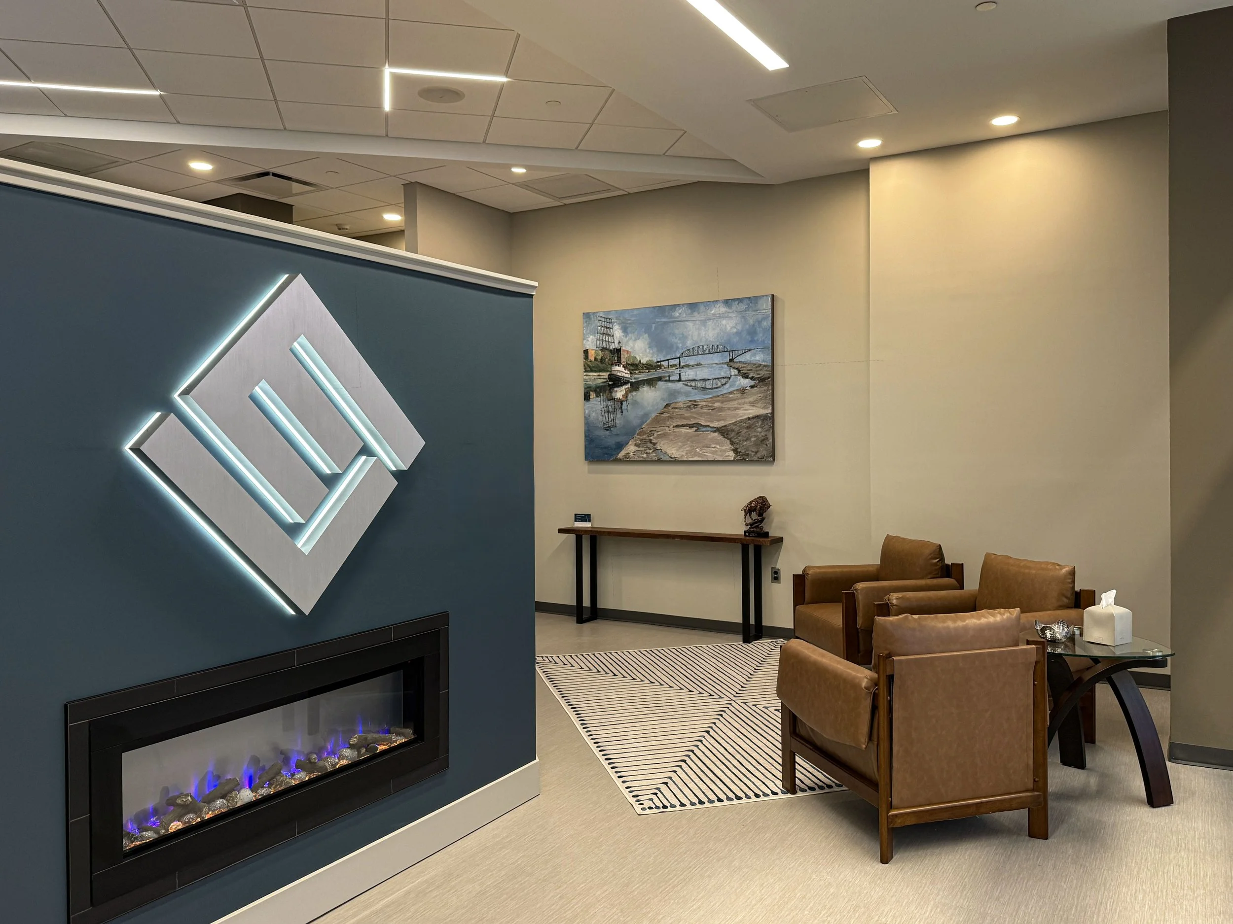Lippes Mathias entry way with a lit up logo over a fireplace and a cluster of brown leather chairs