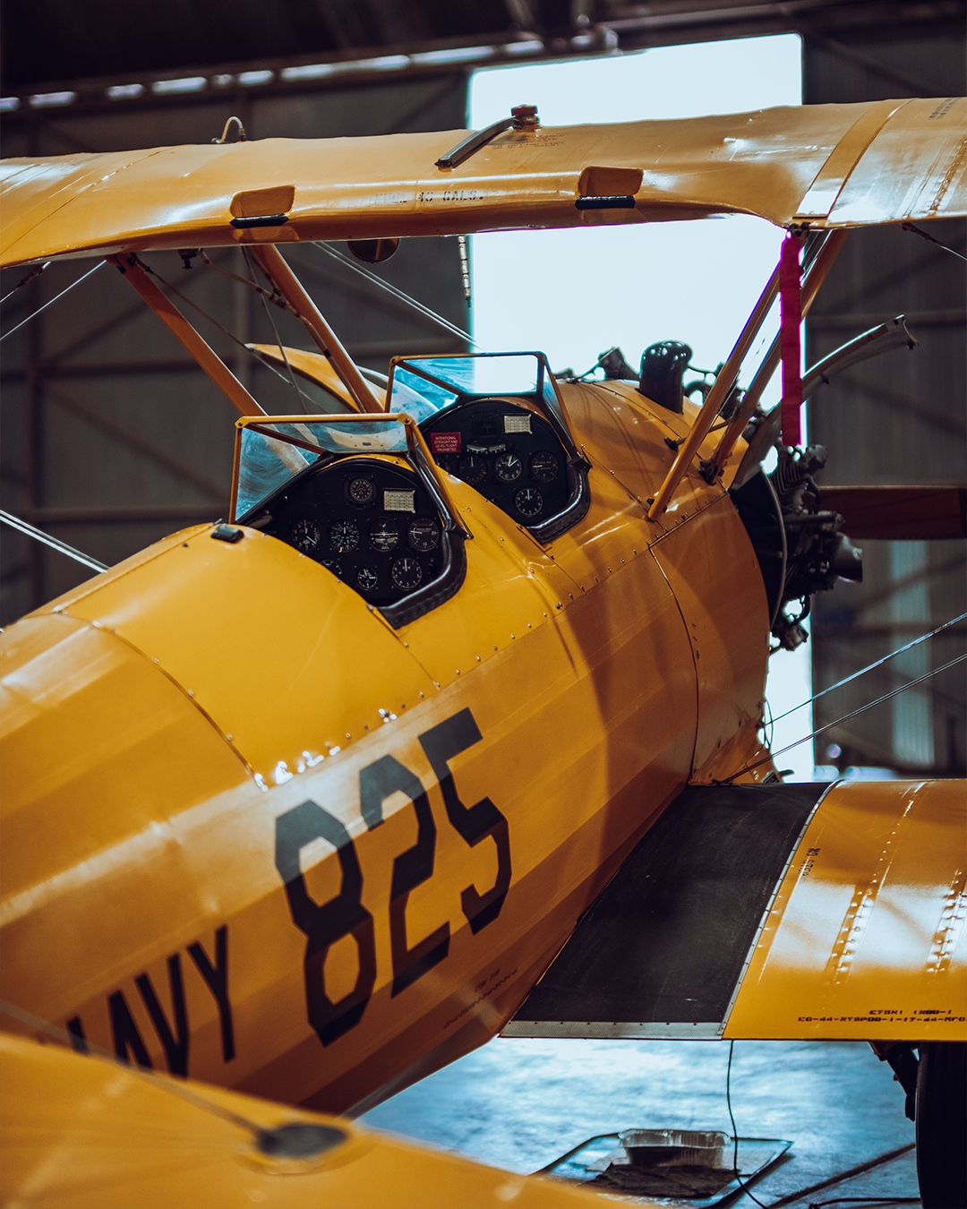 Yellow vintage biplane with "Navy 825" marking inside a hangar.