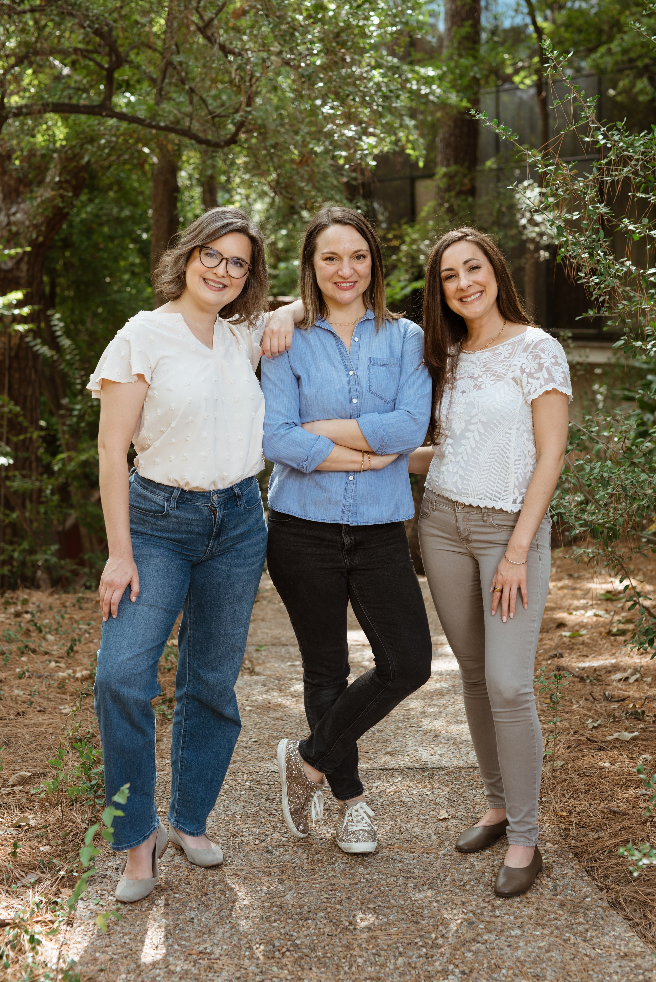 Three Houston therapists standing outdoors on a path, smiling, with trees and greenery in the background.