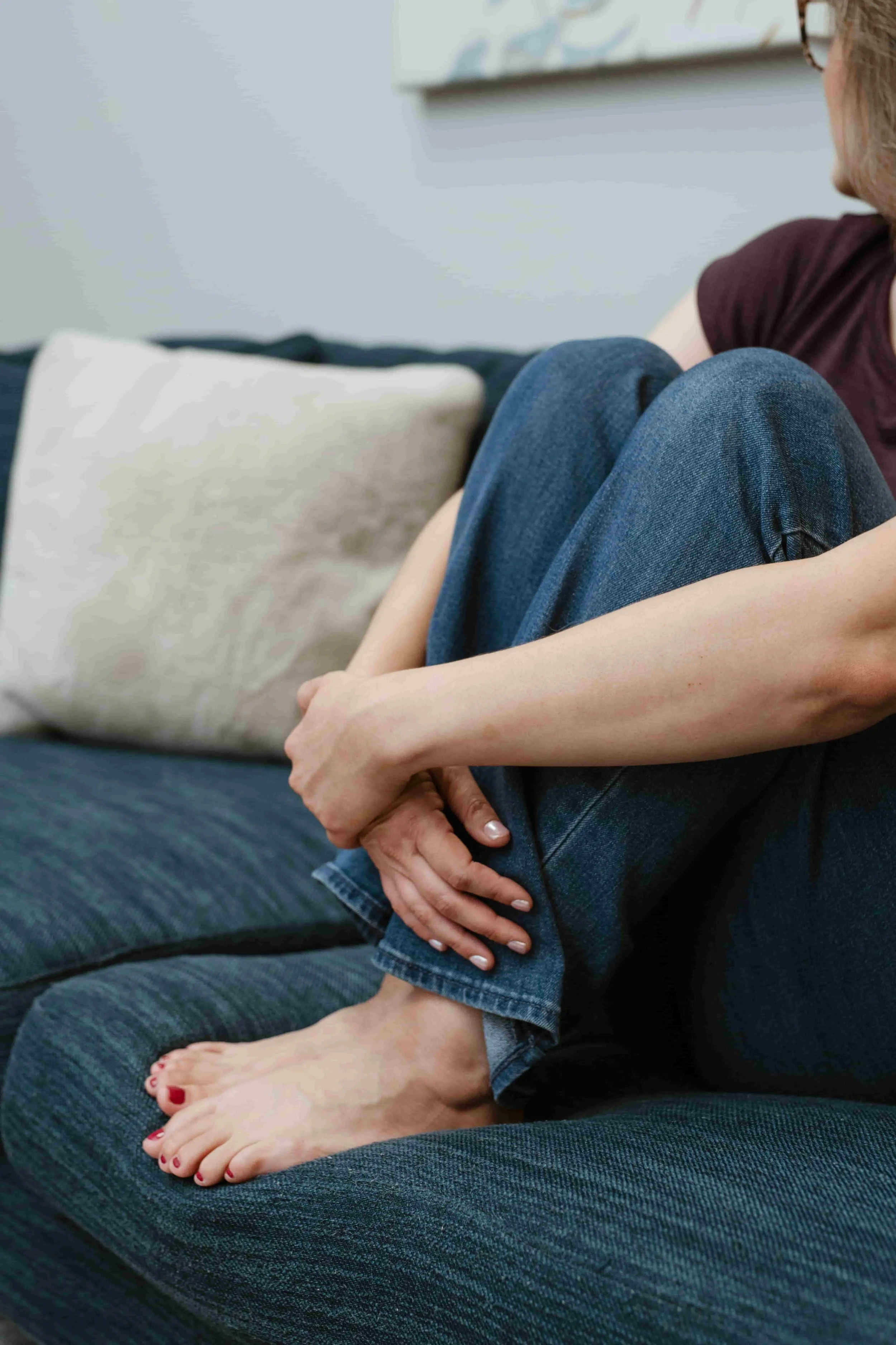A woman sitting on the floor with her head down and arms crossed over her knees in a sign of distress or sadness, in a living room setting.