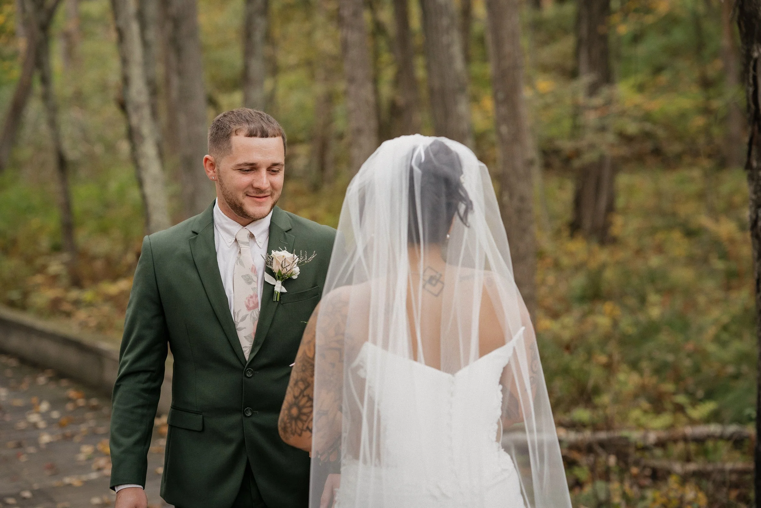 A bride and groom standing outdoors in a wooded area during their wedding.