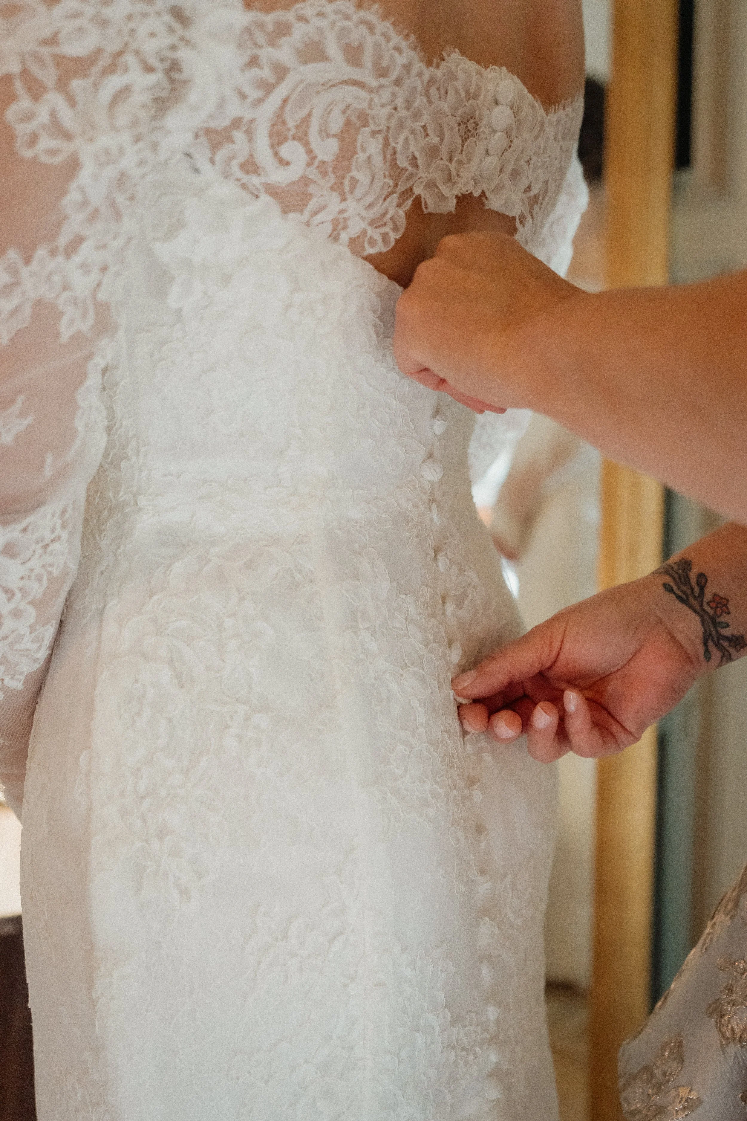 Close-up of a bride's lace wedding dress being buttoned or fastened at the back.