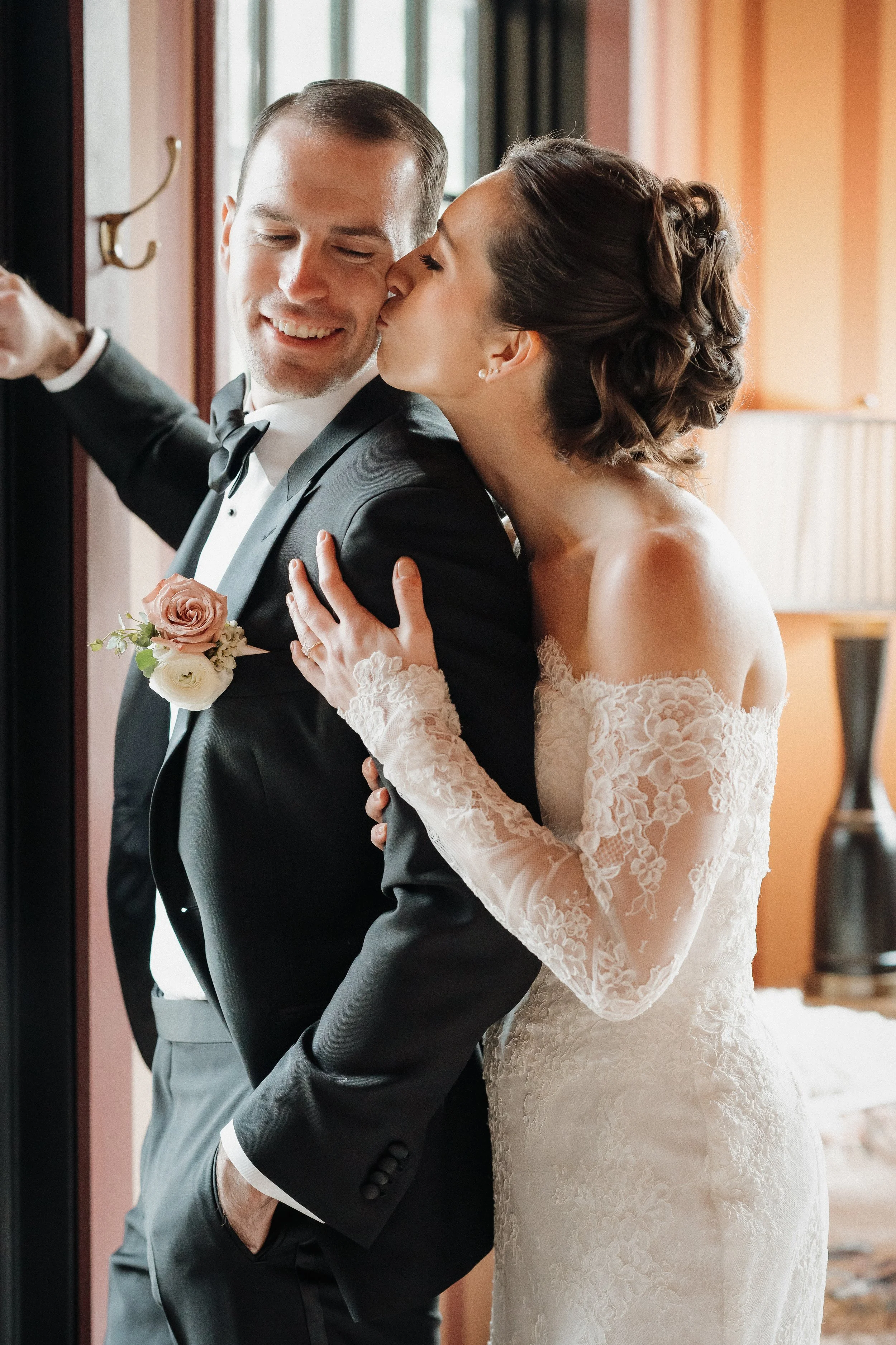 A bride kissing a groom on the cheek in a wedding dress and tuxedo.