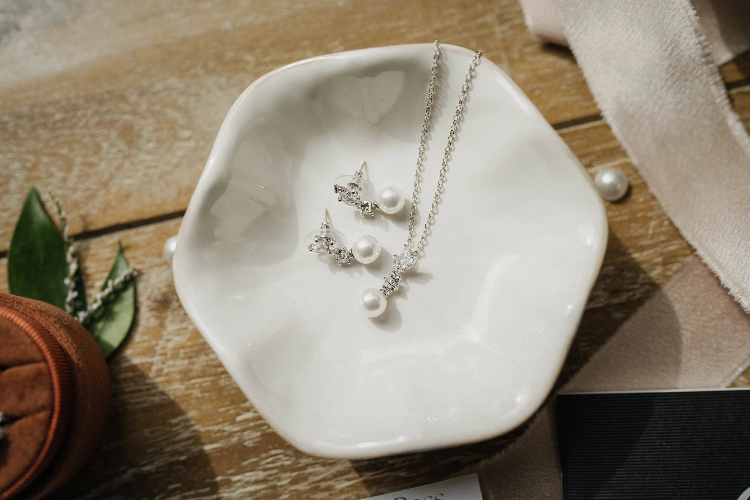 A white ceramic dish with pearl jewelry and a silver necklace on a wooden surface.