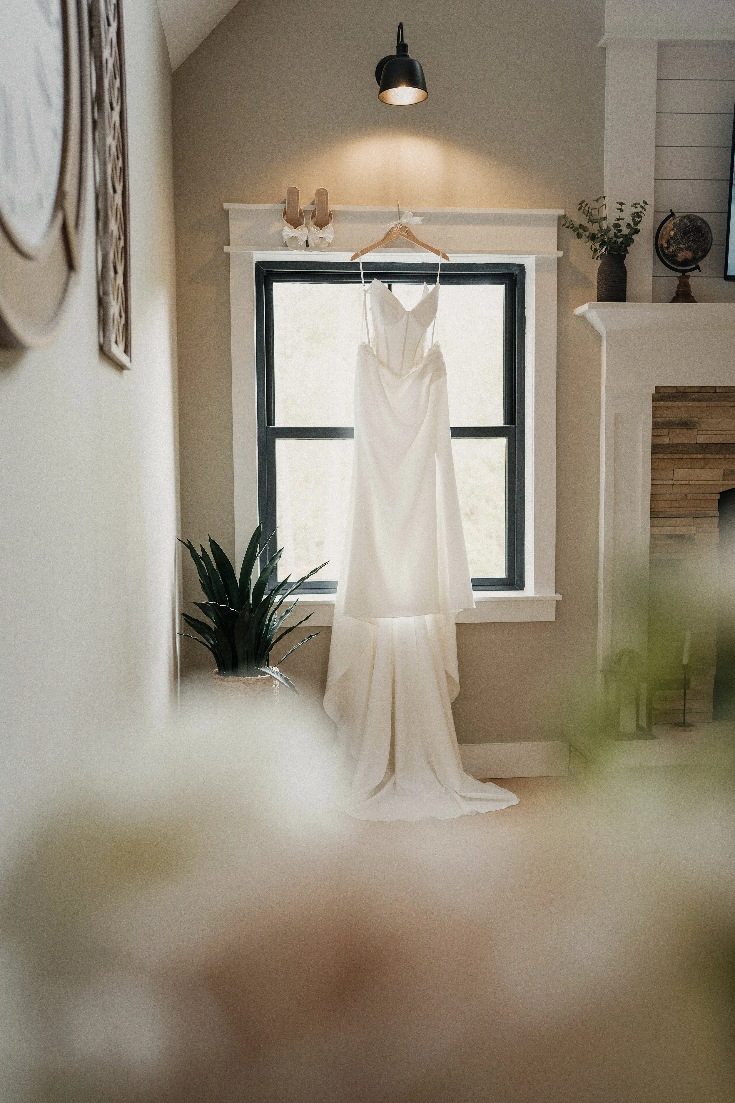 Wedding dress hanging in front of a window in a cozy room with beige walls and minimal decor.