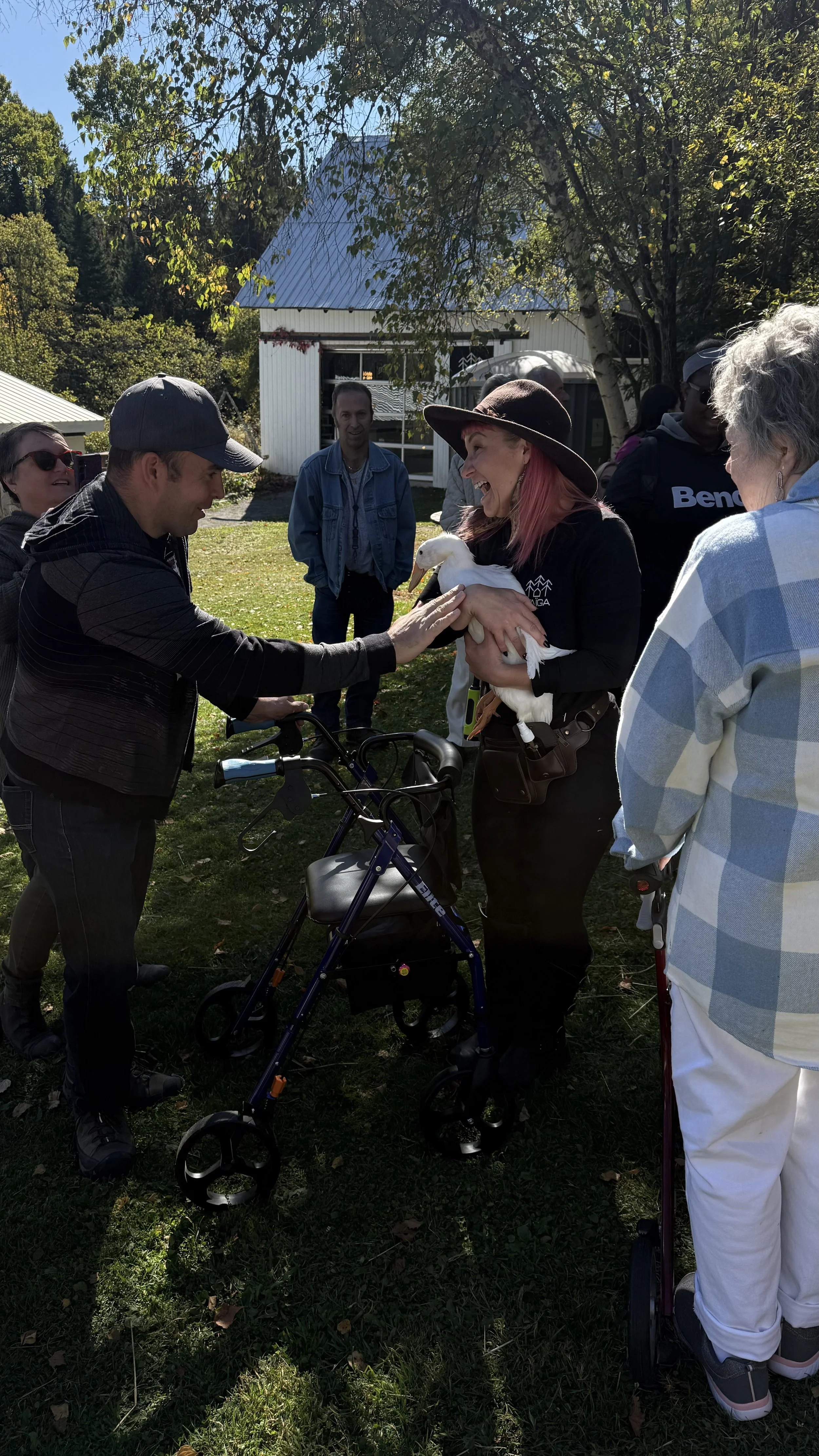 Groupe de personnes en extérieur, dont une femme avec un chapeau noir et une femme avec un albinose, qui tiennent un petit animal blanchi, probablement un oiseau ou un petit animal.