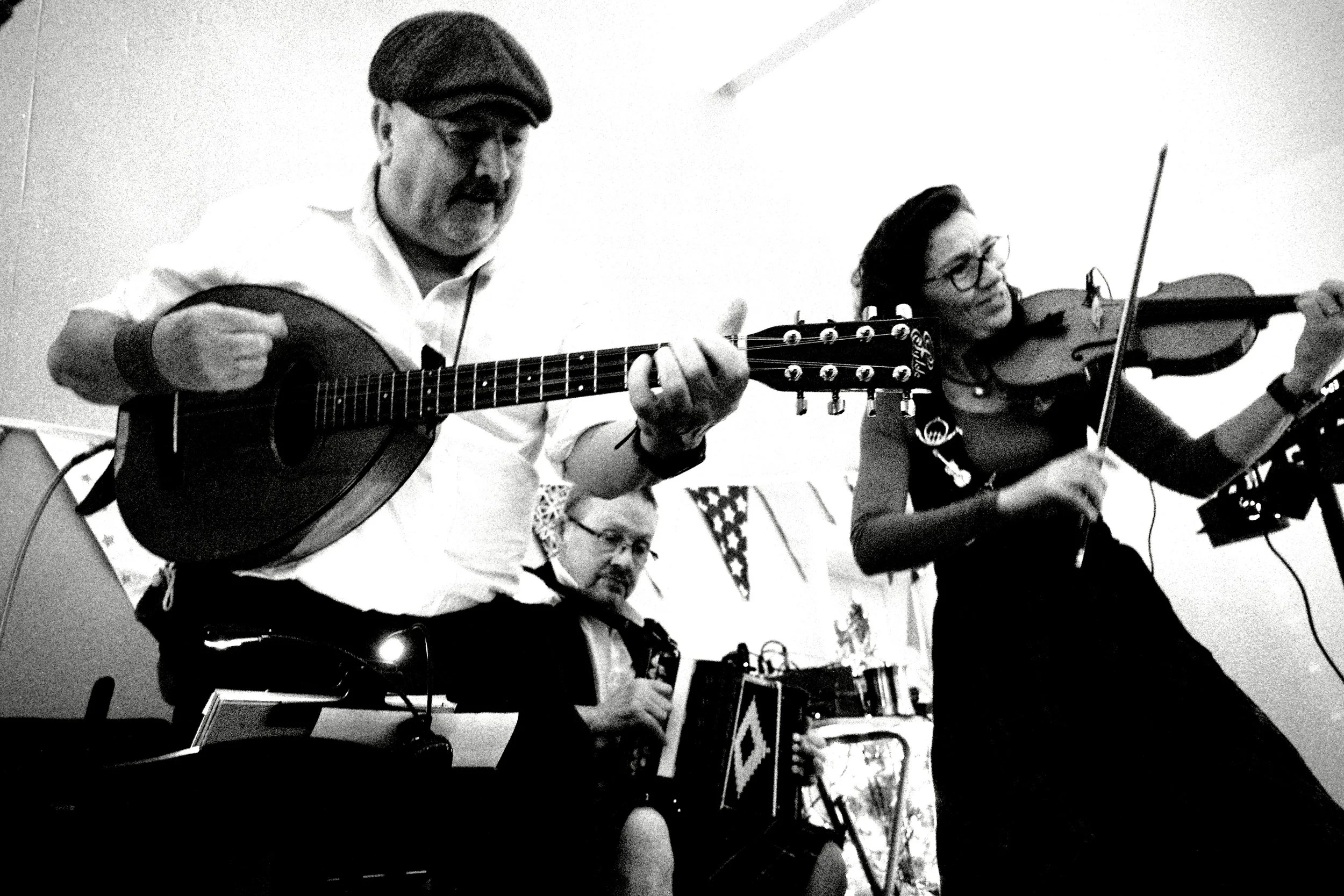 Three musicians performing indoors; one playing guitar, one on violin, another on an accordion.